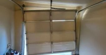 Garage door, partially open and crooked, in a beige-walled garage.