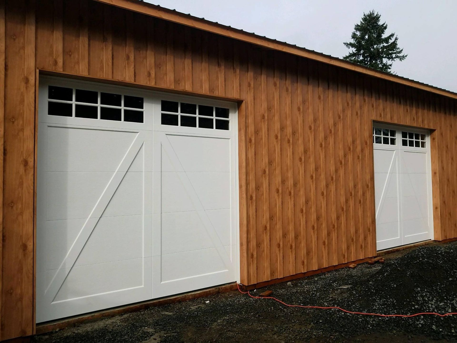 Two white garage doors with windows, on a wooden building.