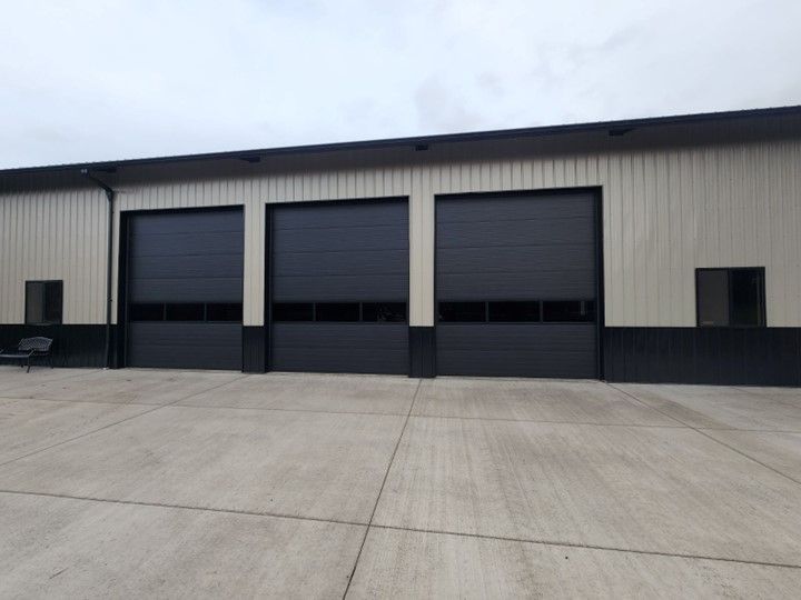 Three closed black garage doors on a light-colored industrial building with a concrete apron.