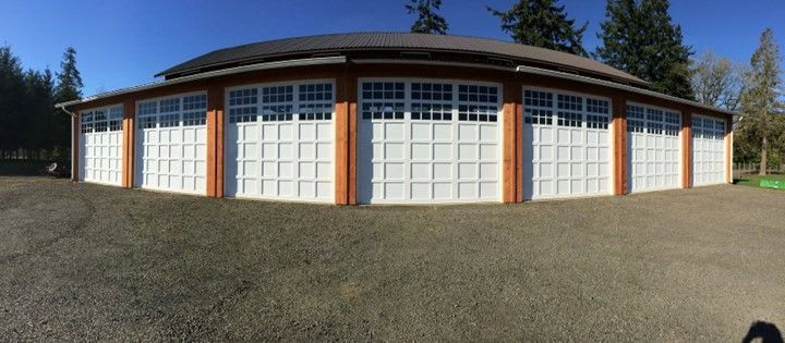 A circular building with white garage doors, orange trim, and a gray roof on a gravel lot.