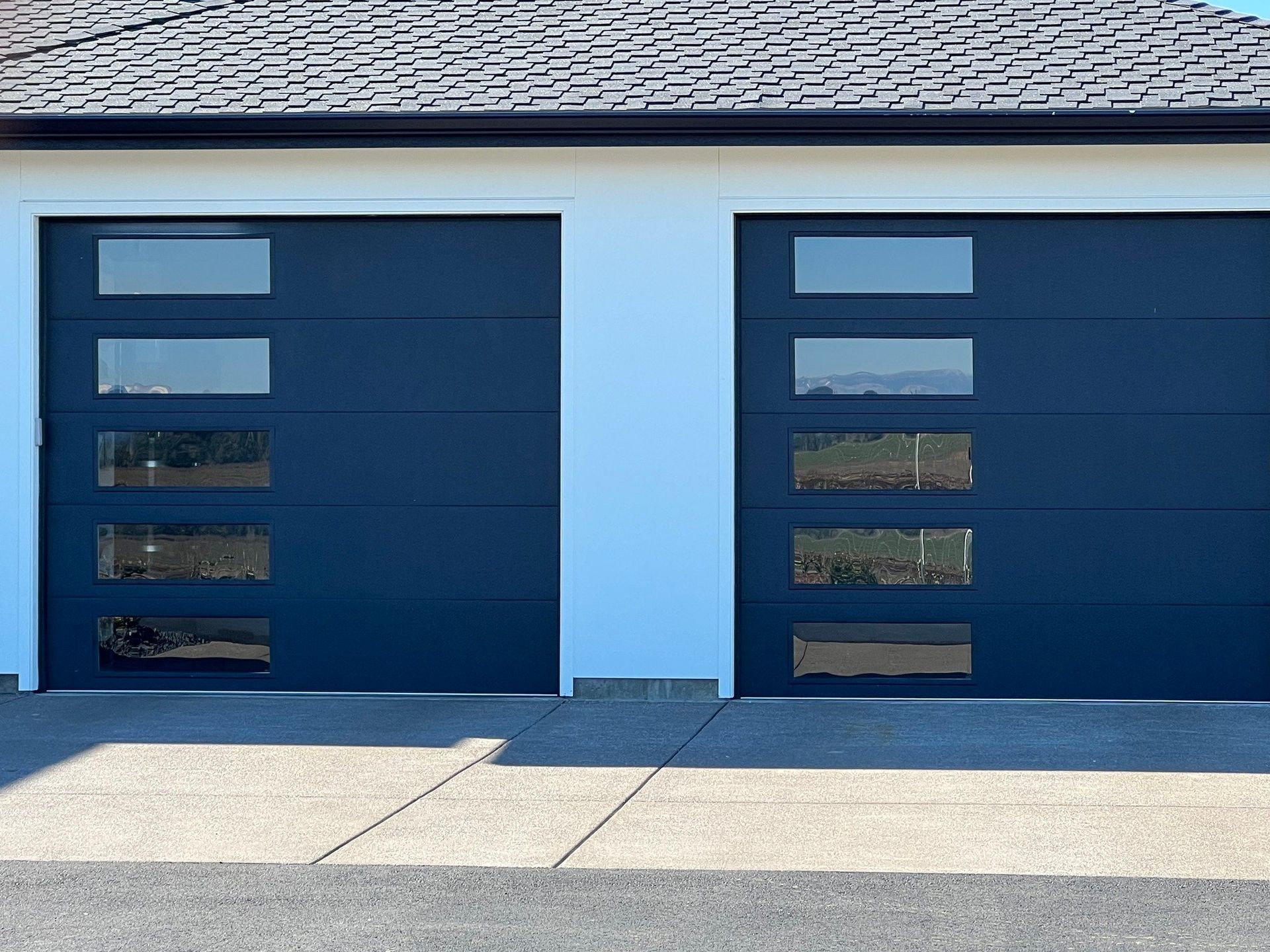 Two blue garage doors with rectangular windows, set in a white frame, on a concrete driveway.
