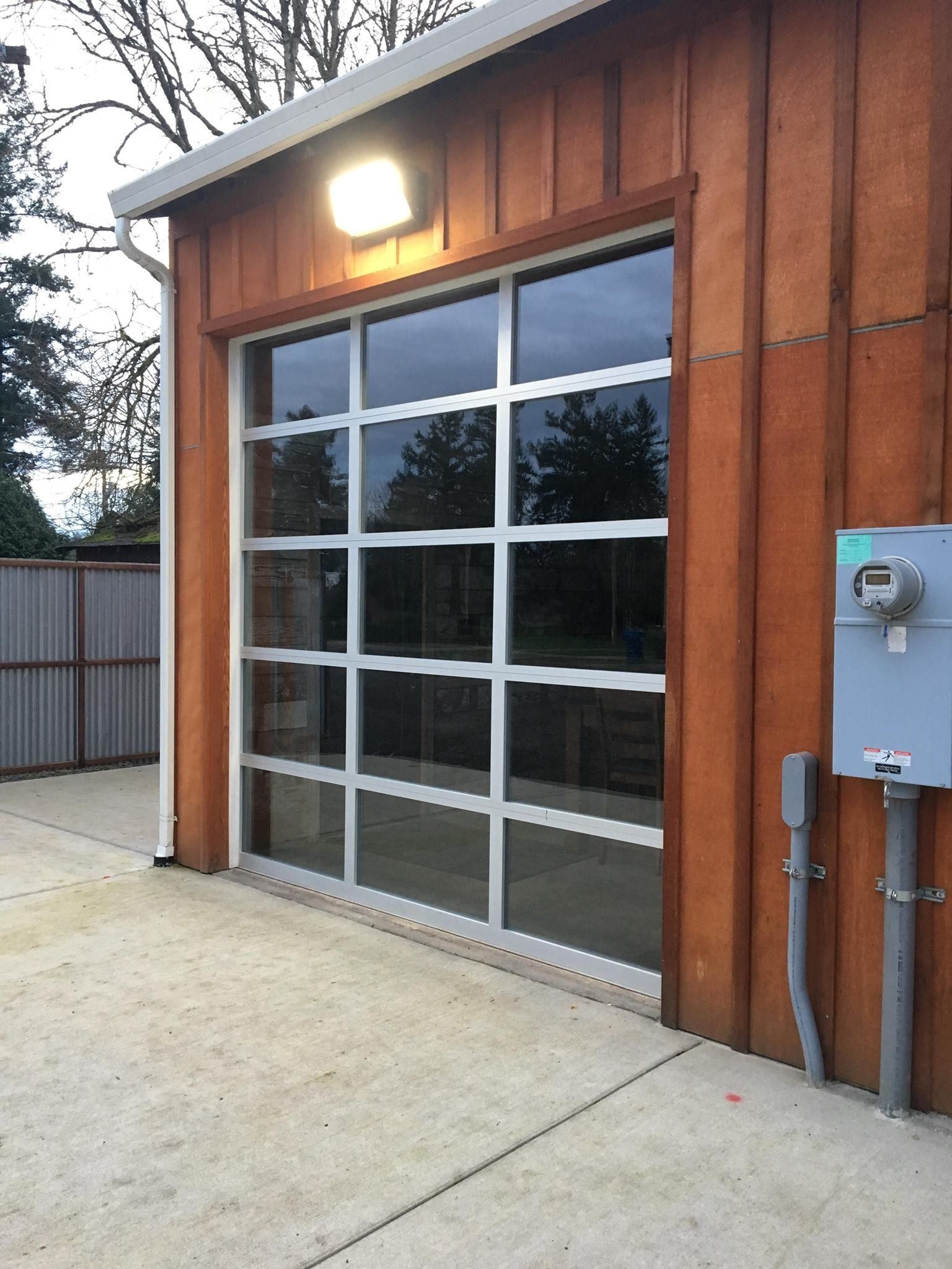 Glass garage door with grid, on a brown wooden building, with an exterior light and concrete floor.