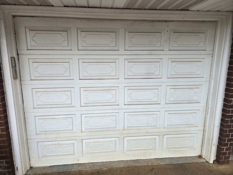 White garage door with rectangular panels, dirt stains, brick sides.