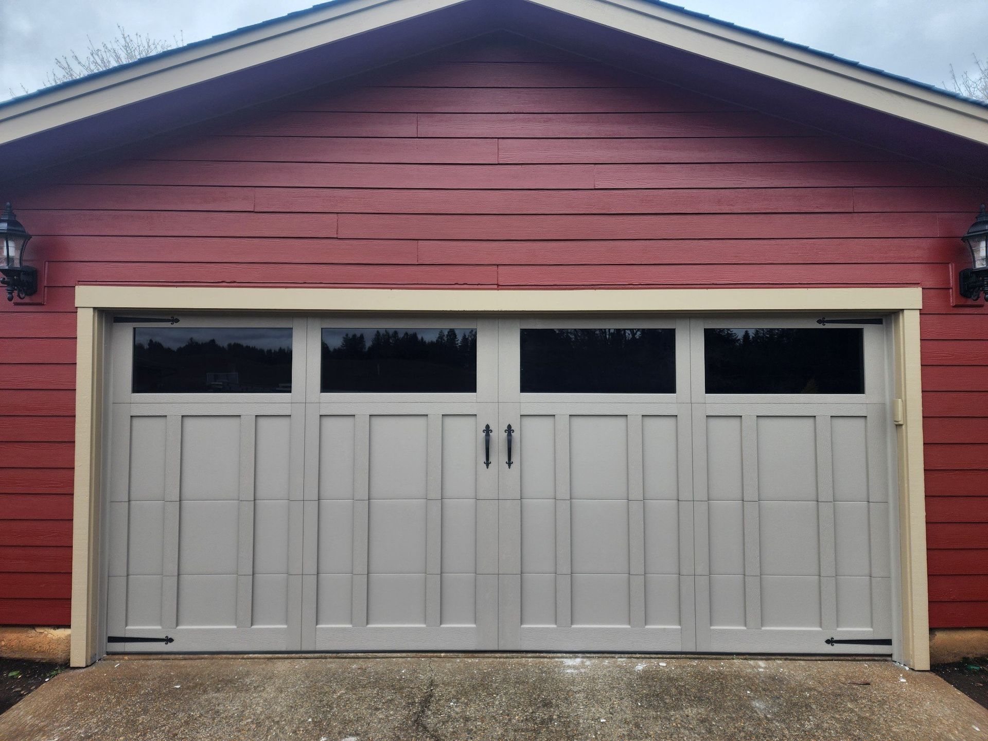 Gray garage door with four window panels, set in a red building with tan trim.