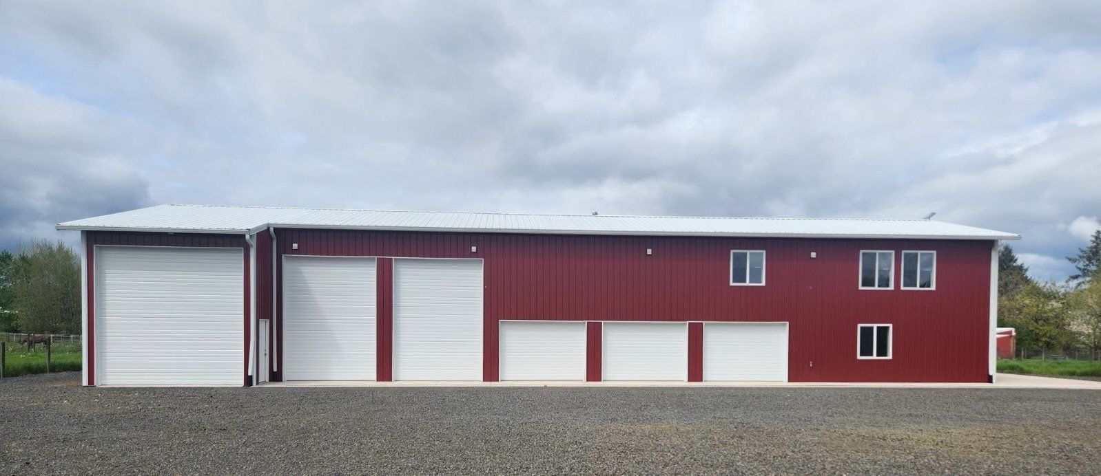Red metal building with white garage doors and windows under a cloudy sky.