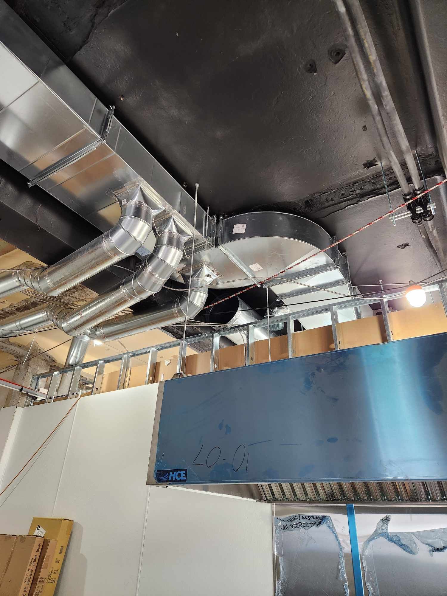 Plafond industriel avec conduits apparents, tuyauterie métallique et grand panneau bleu en construction