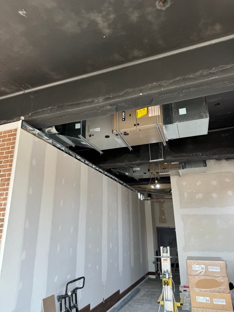 Pièce intérieure partiellement aménagée avec conduits de plafond apparents, cloisons sèches, outils et boîtes empilées