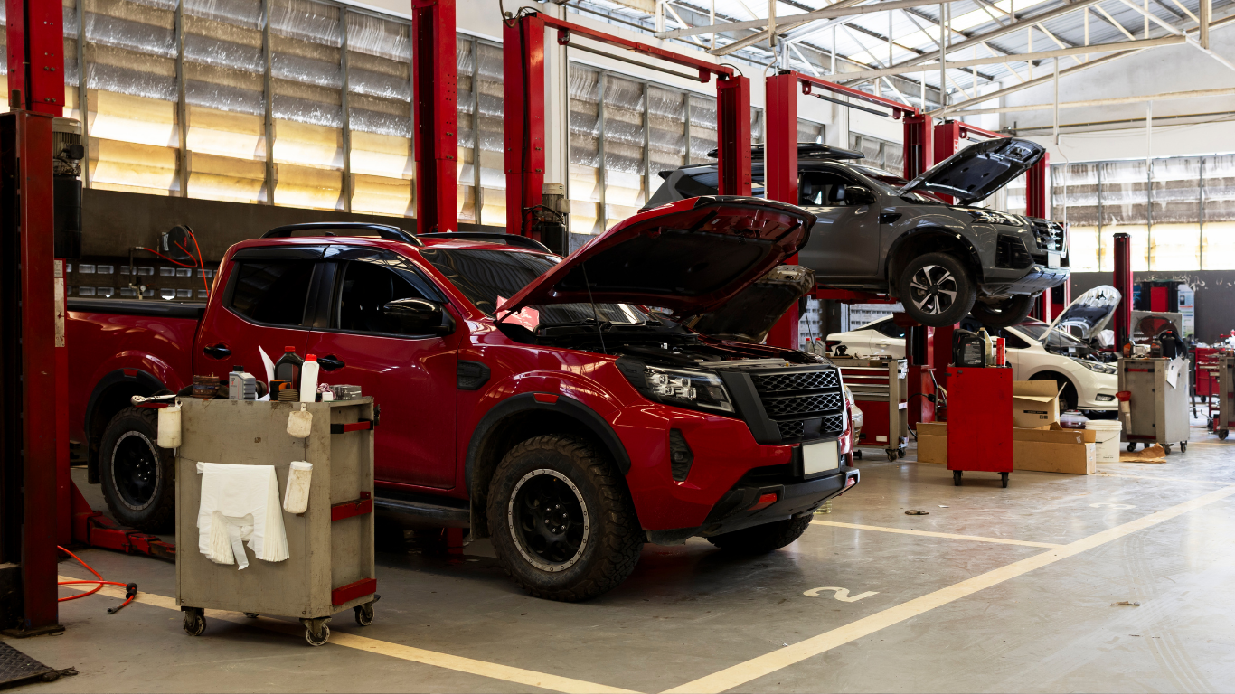 Red SUV on an assembly line in an auto factory, with another vehicle lifted overhead
