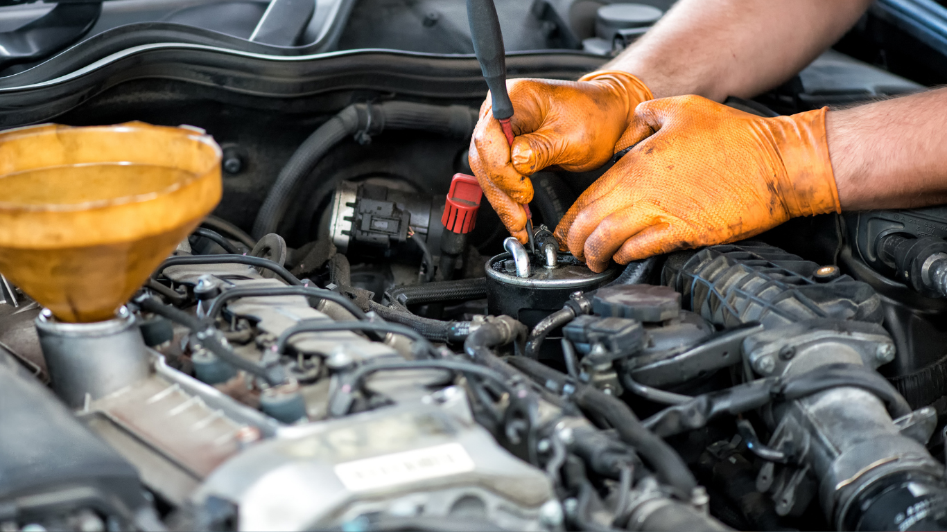 Mechanic’s gloved hands working on a car engine with a funnel and oil cap open