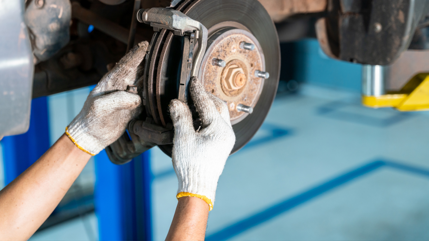 Mechanic’s gloved hands replacing brake pads on a car wheel in a garage