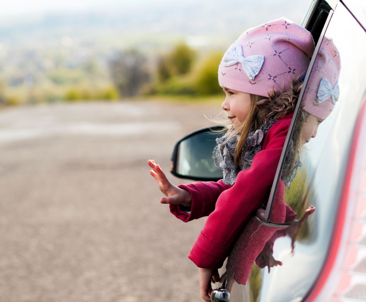 A little girl in a pink hat is looking out of a car window.