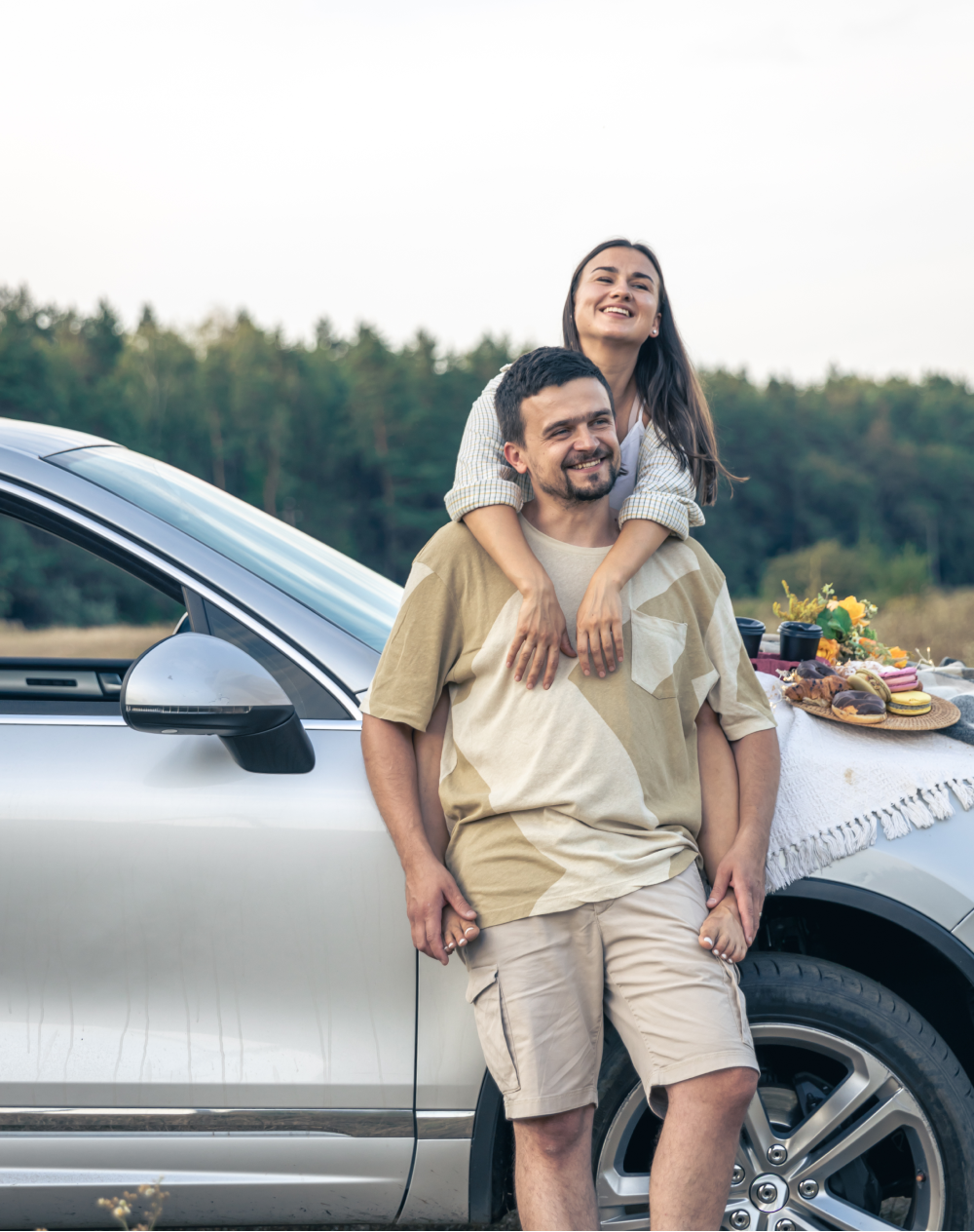 A man is carrying a woman on his shoulders while standing next to a car.