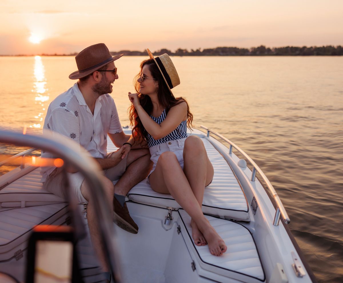 A man and a woman are sitting on a boat in the water at sunset.