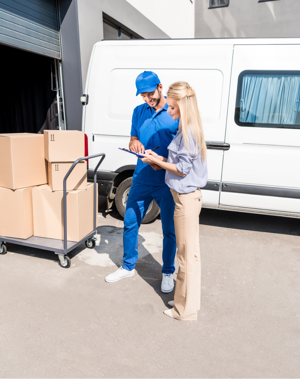 A man and a woman are looking at a tablet in front of a van filled with boxes.