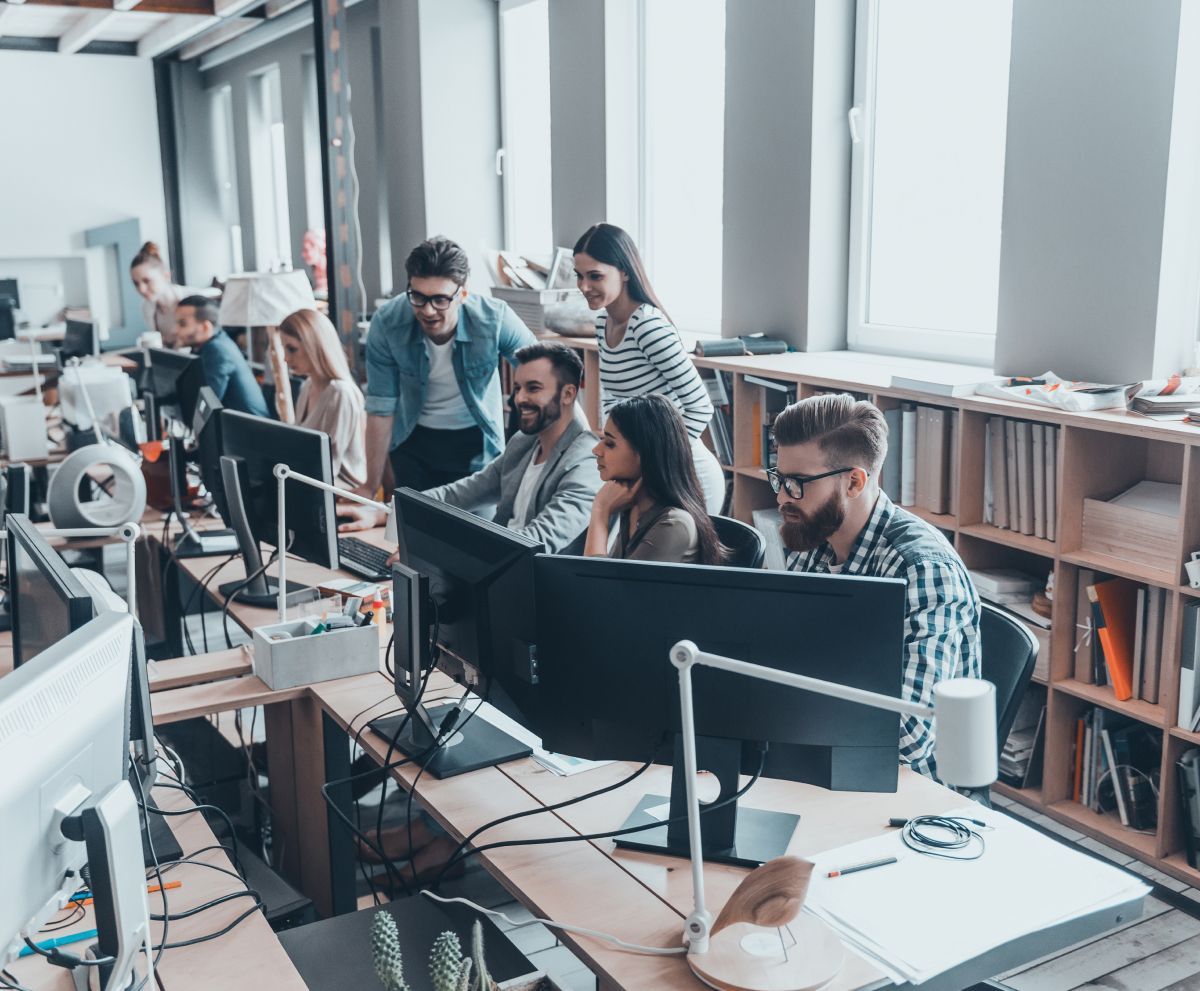 A group of people are sitting at desks in front of computer monitors in an office.