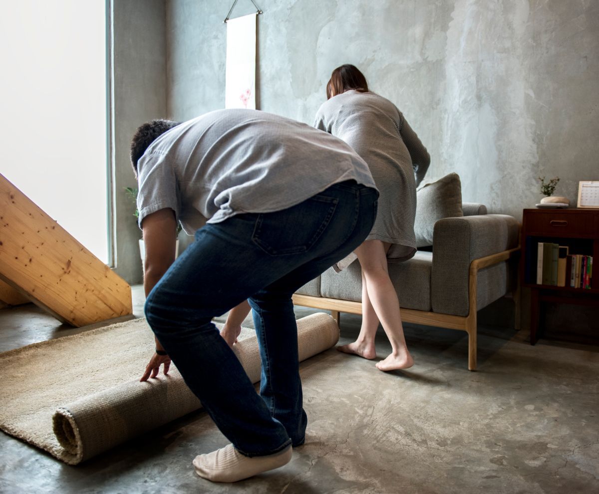 A man and a woman are rolling a rug in a living room.