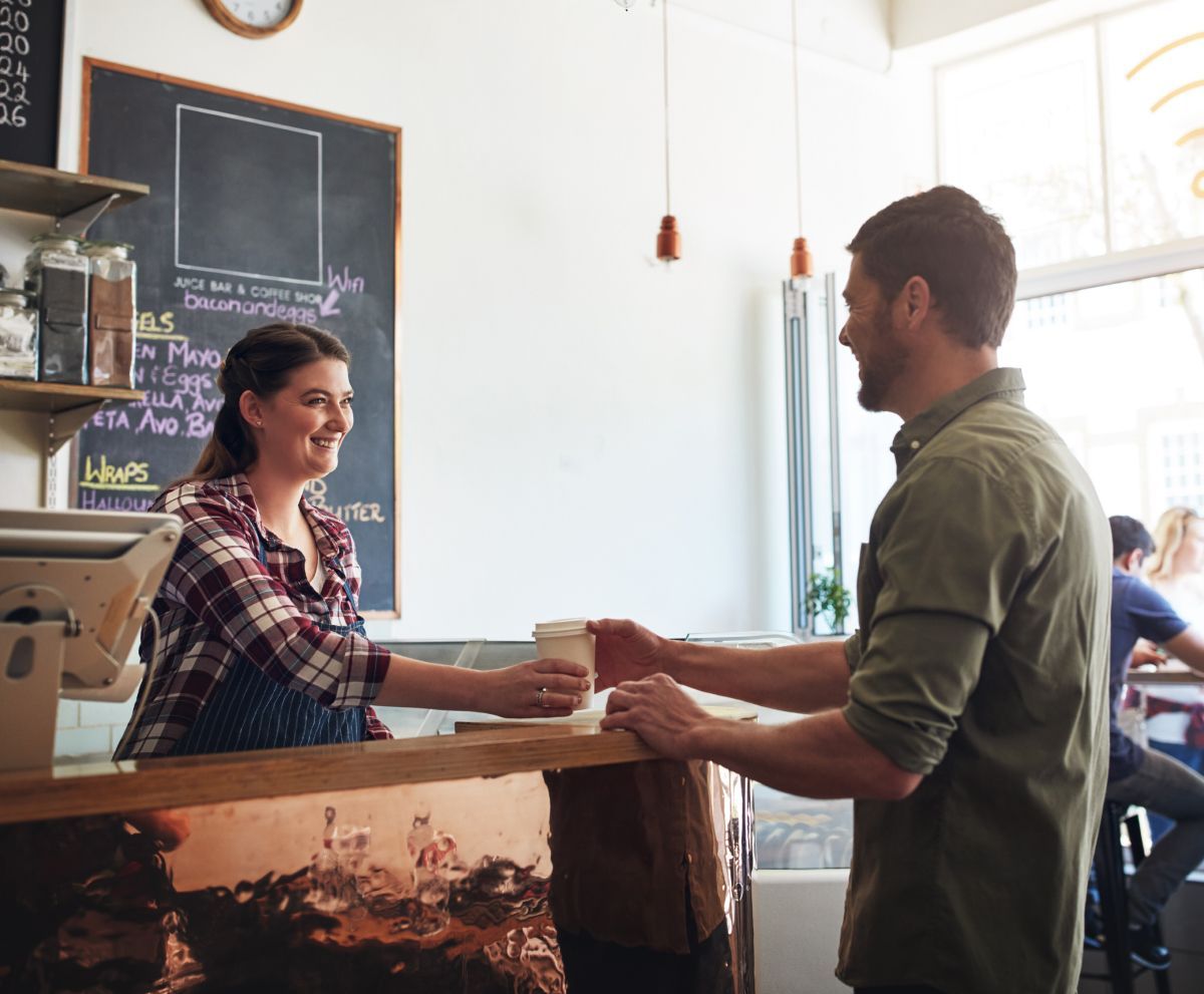 A man is getting a cup of coffee from a woman at a counter in a restaurant.