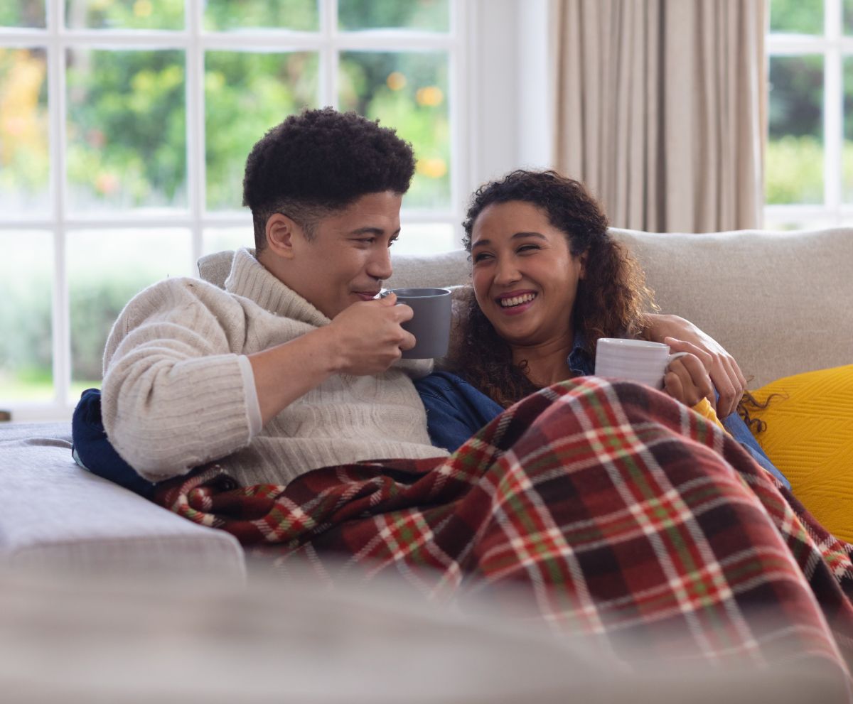 A man and a woman are sitting on a couch with a plaid blanket.