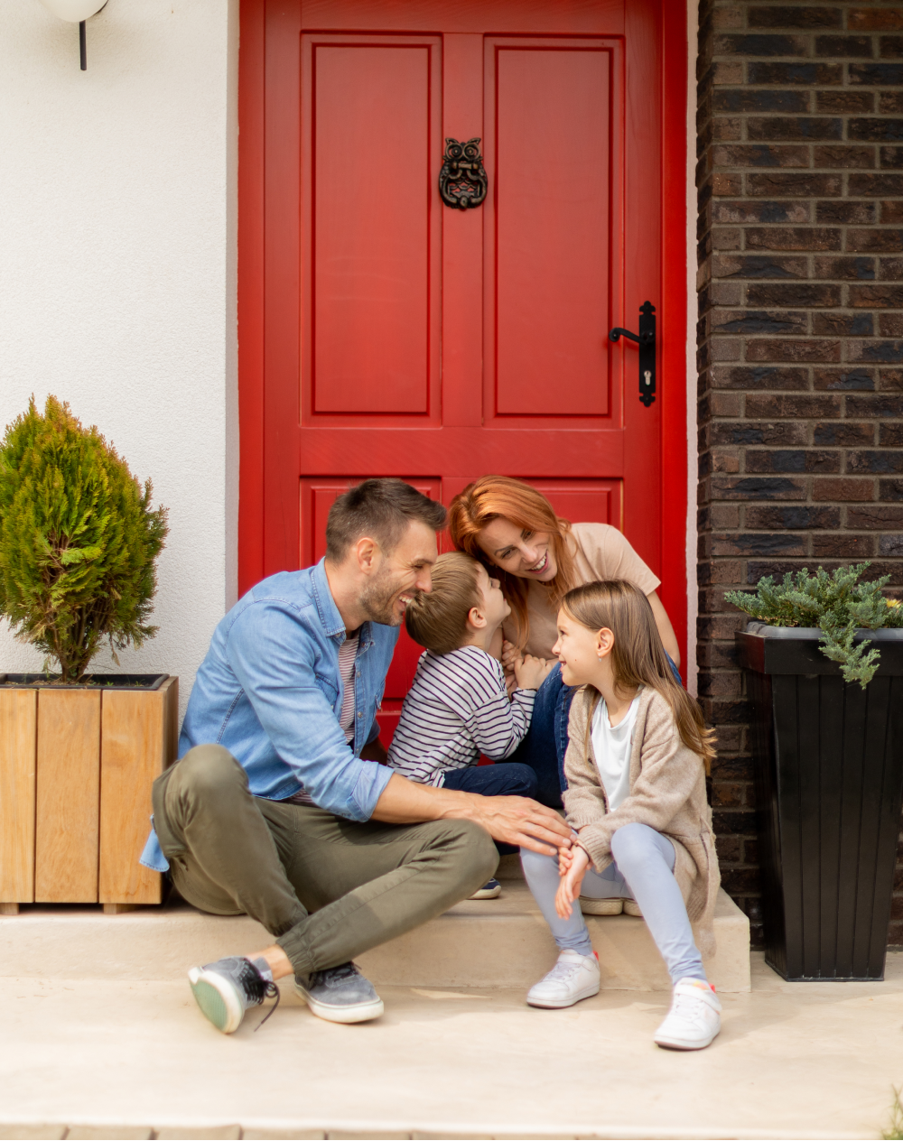 A family is sitting on the steps of their house in front of a red door.
