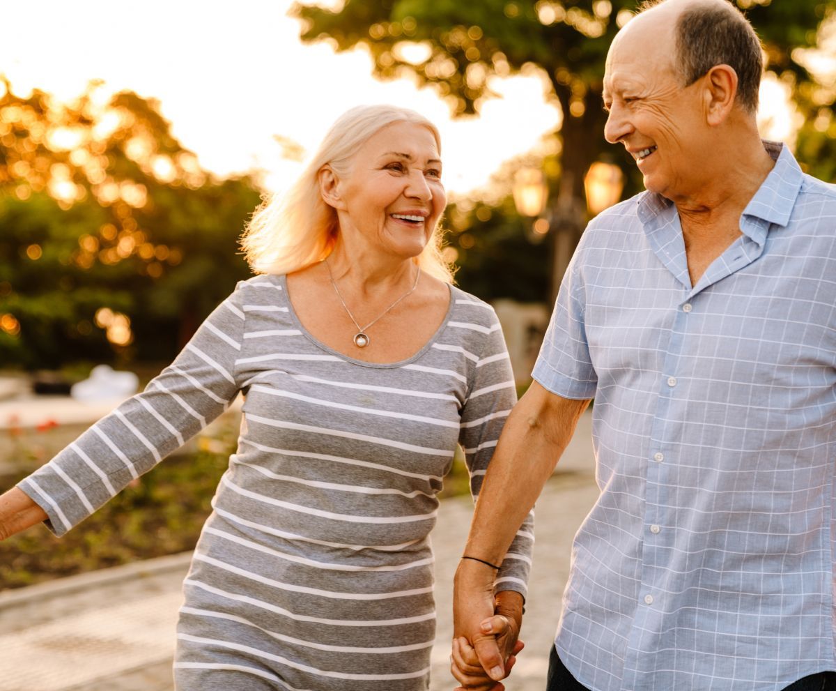 A man and a woman are holding hands while walking down a sidewalk.