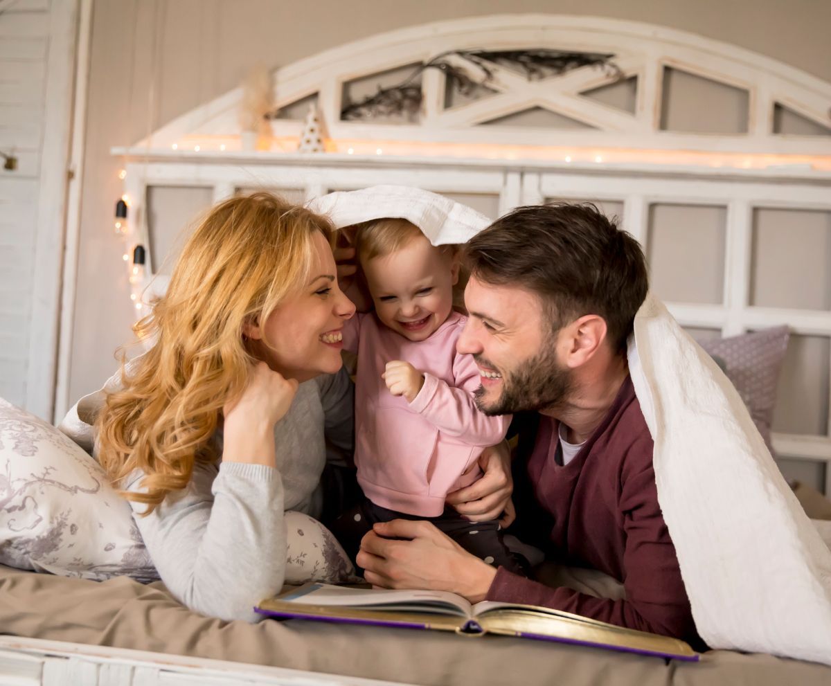 A man and woman are laying on a bed with a baby.