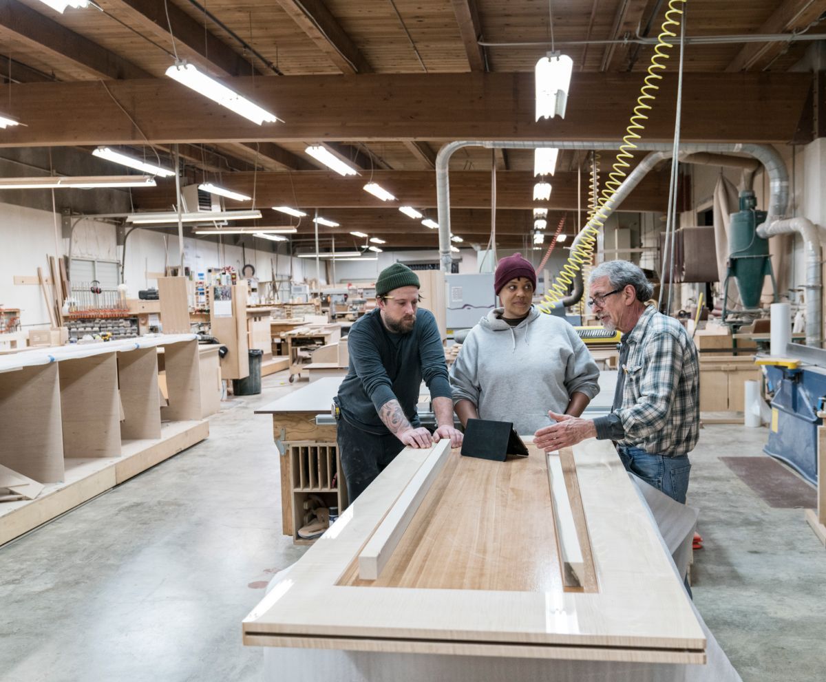 A group of people are standing around a wooden table in a factory.