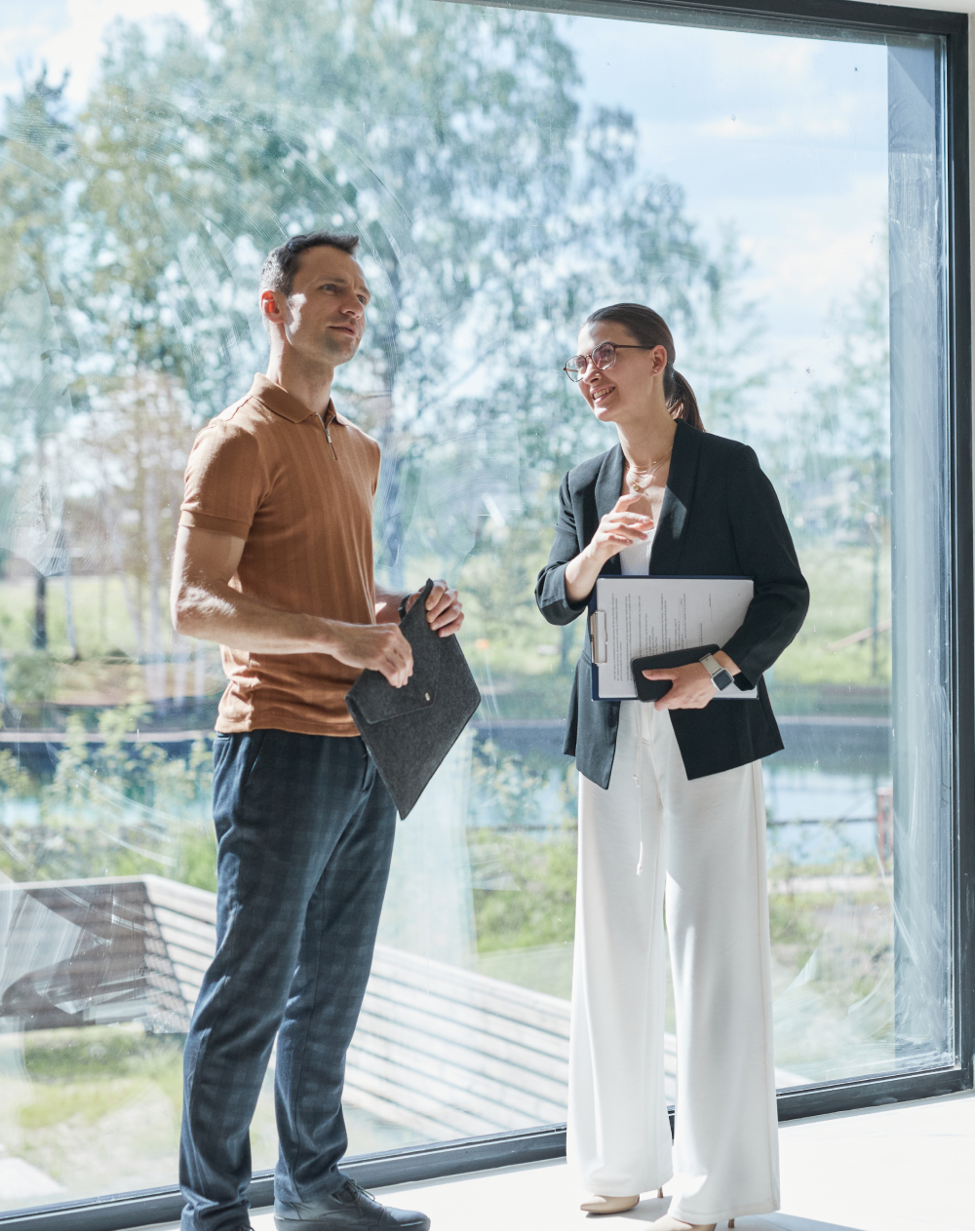 A man and a woman are standing next to each other in front of a large window.