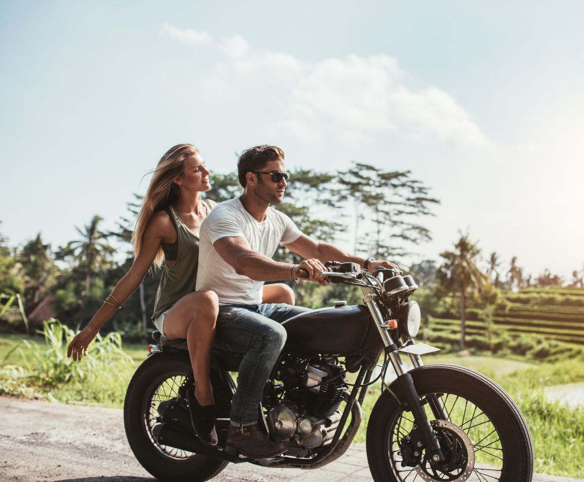 A man and a woman are riding a motorcycle down a dirt road.