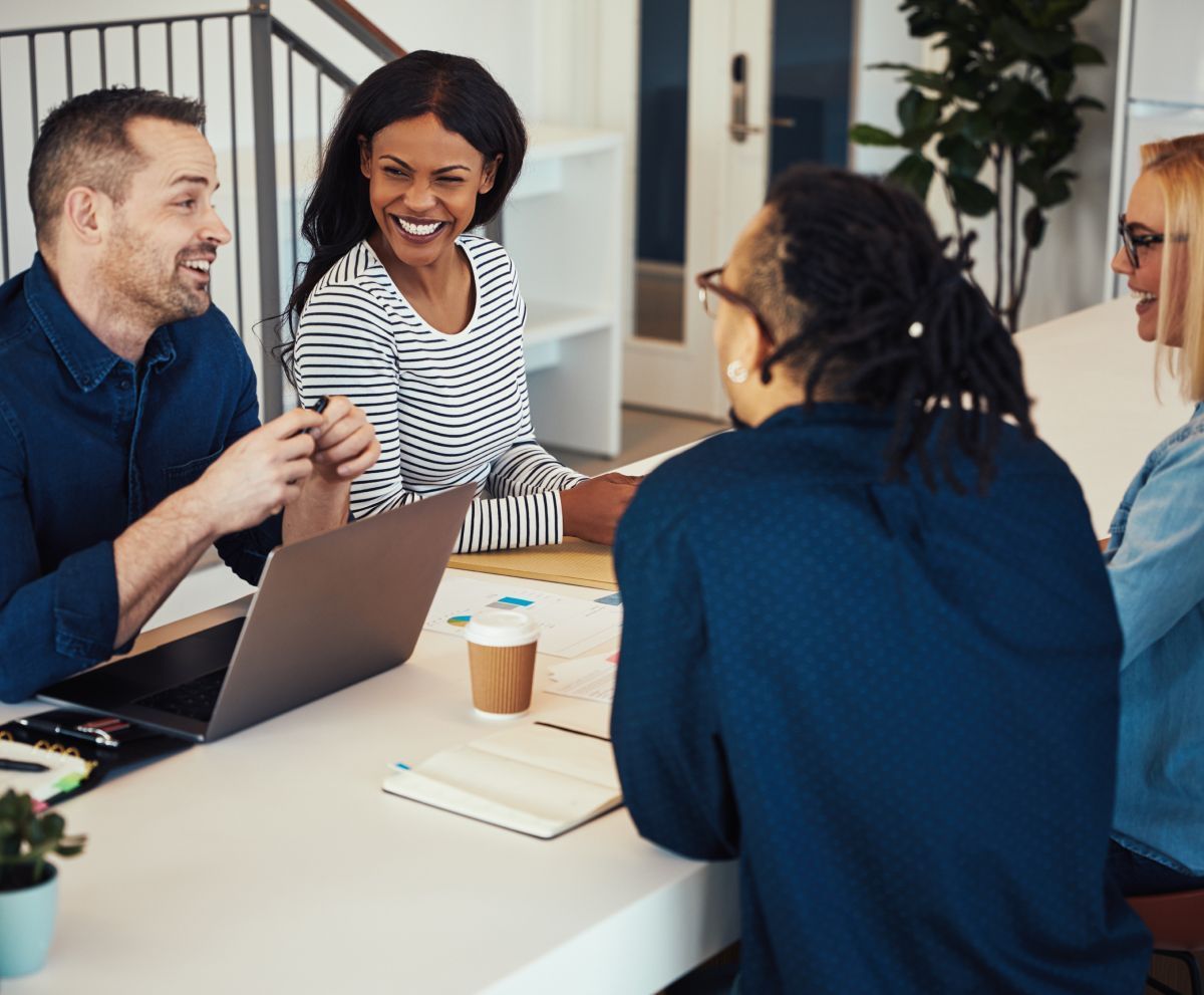 A group of people are sitting around a table with a laptop.