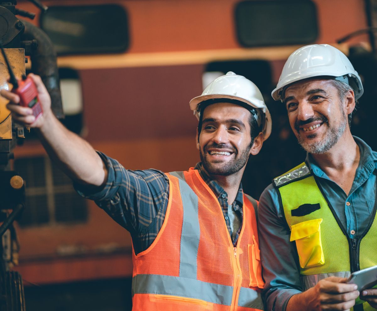 Two construction workers are taking a selfie in a factory.
