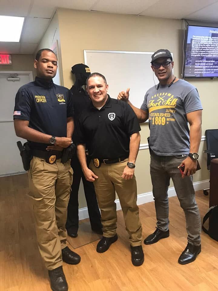Three uniformed people standing together indoors, smiling in front of a whiteboard.
