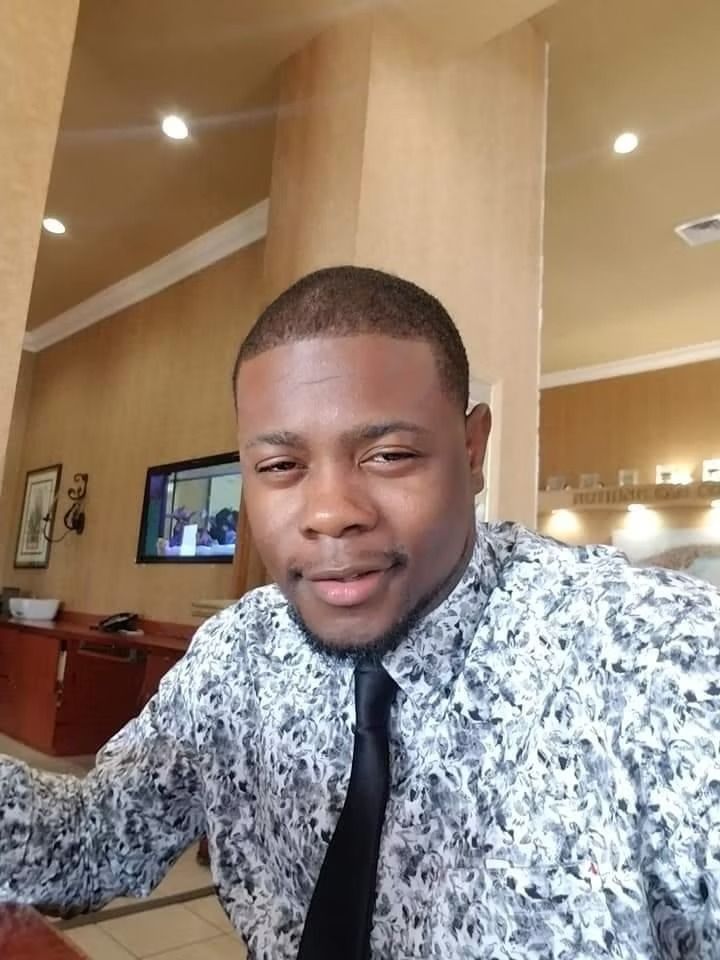 Man in patterned shirt and black tie smiling in a warmly lit restaurant