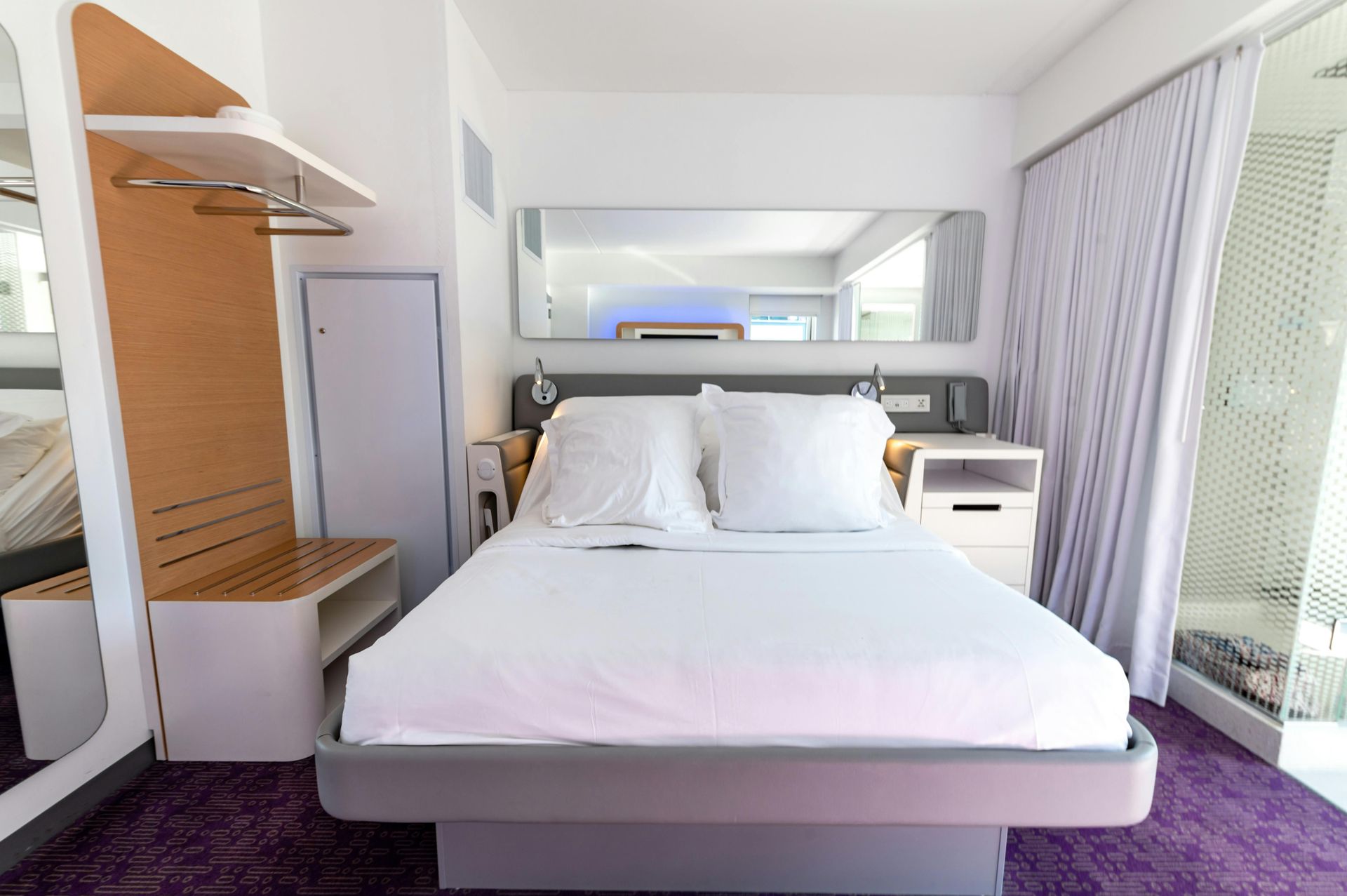 Modern hotel room with a neatly made bed, purple carpet, and balcony doors letting in bright light
