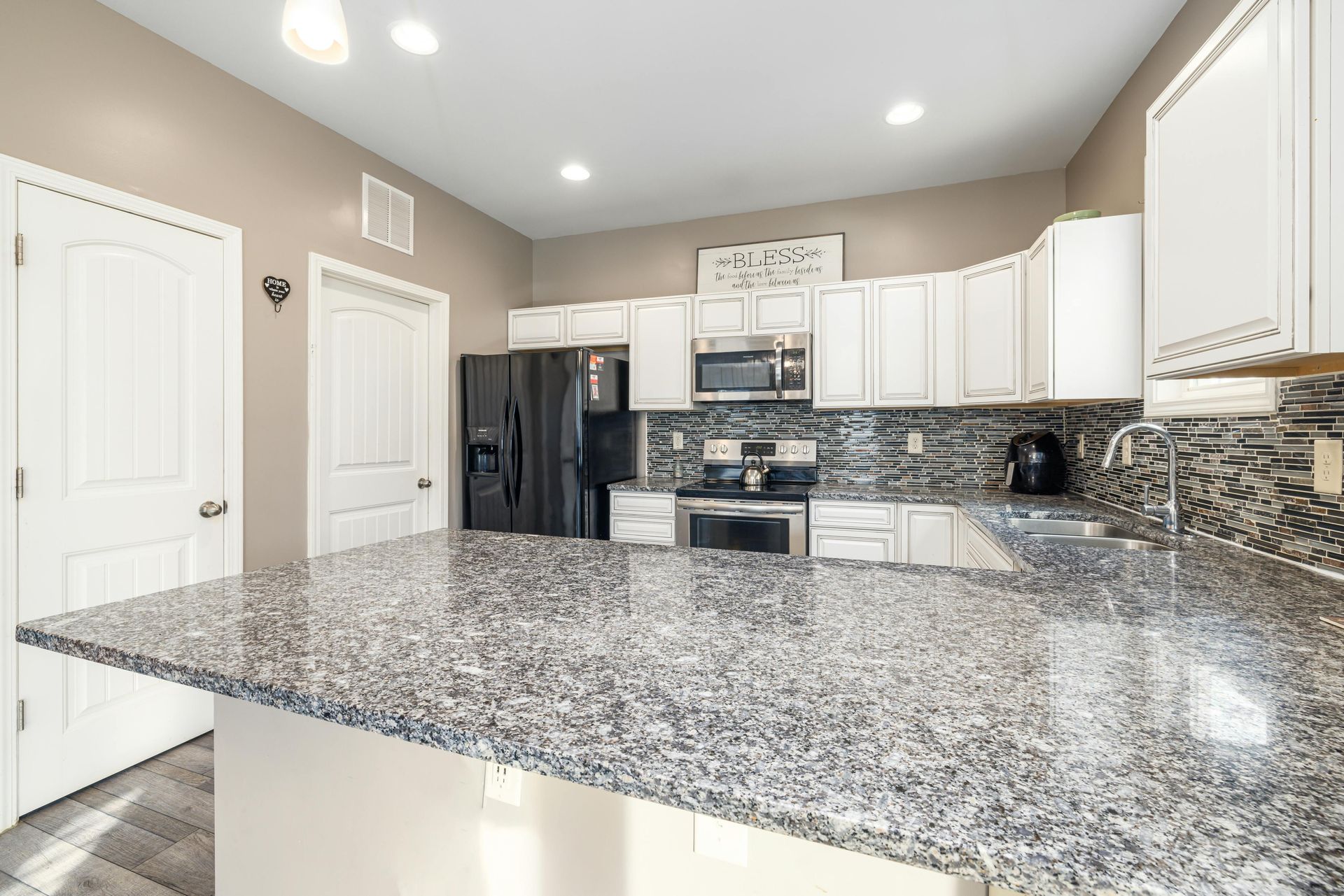 Modern kitchen with white cabinets, black appliances, and a speckled granite countertop