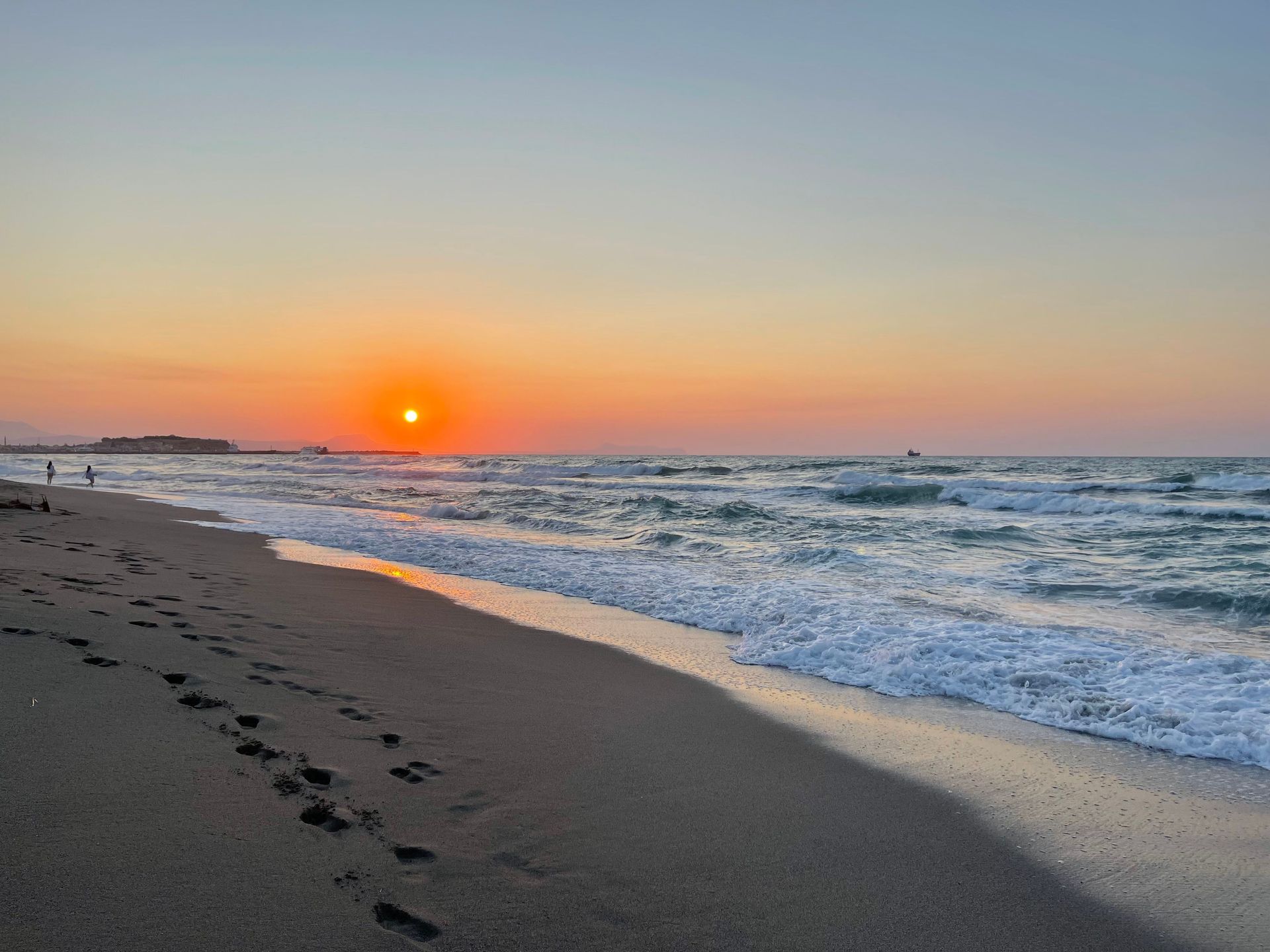 Sunset over a calm beach with footprints in the sand and waves under an orange sky