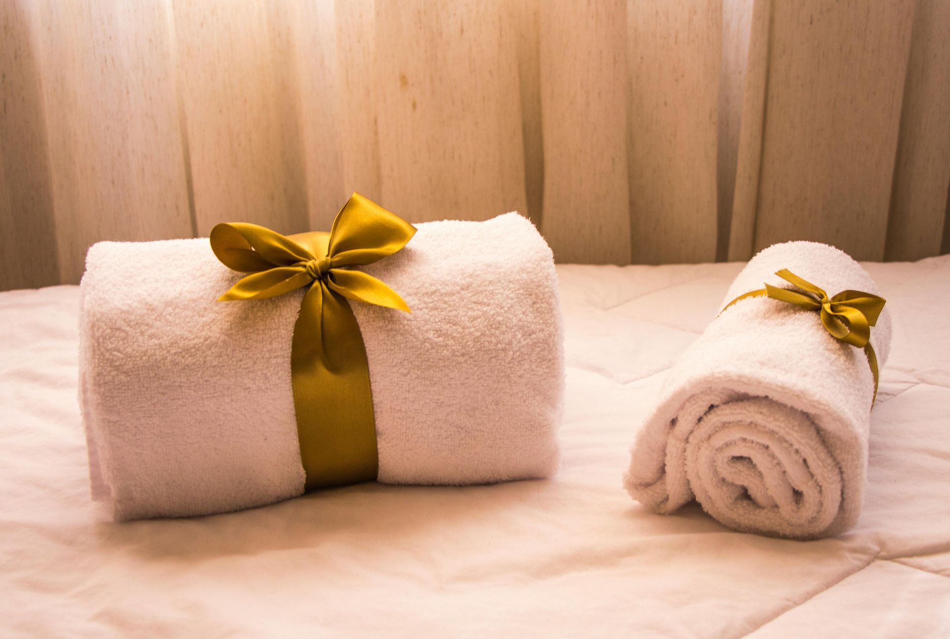 Two white rolled towels tied with gold ribbon on a white bed in a spa setting