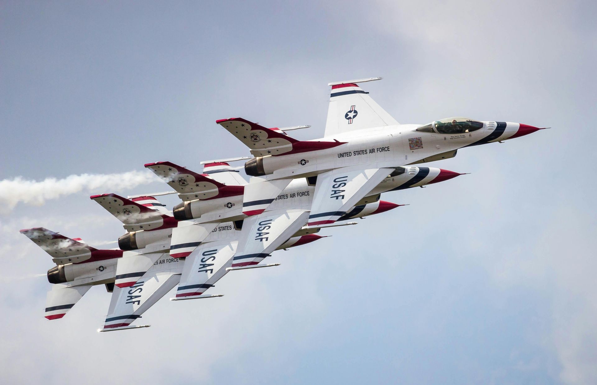 Four white fighter jets flying in formation against a cloudy sky, red-tipped wings visible.