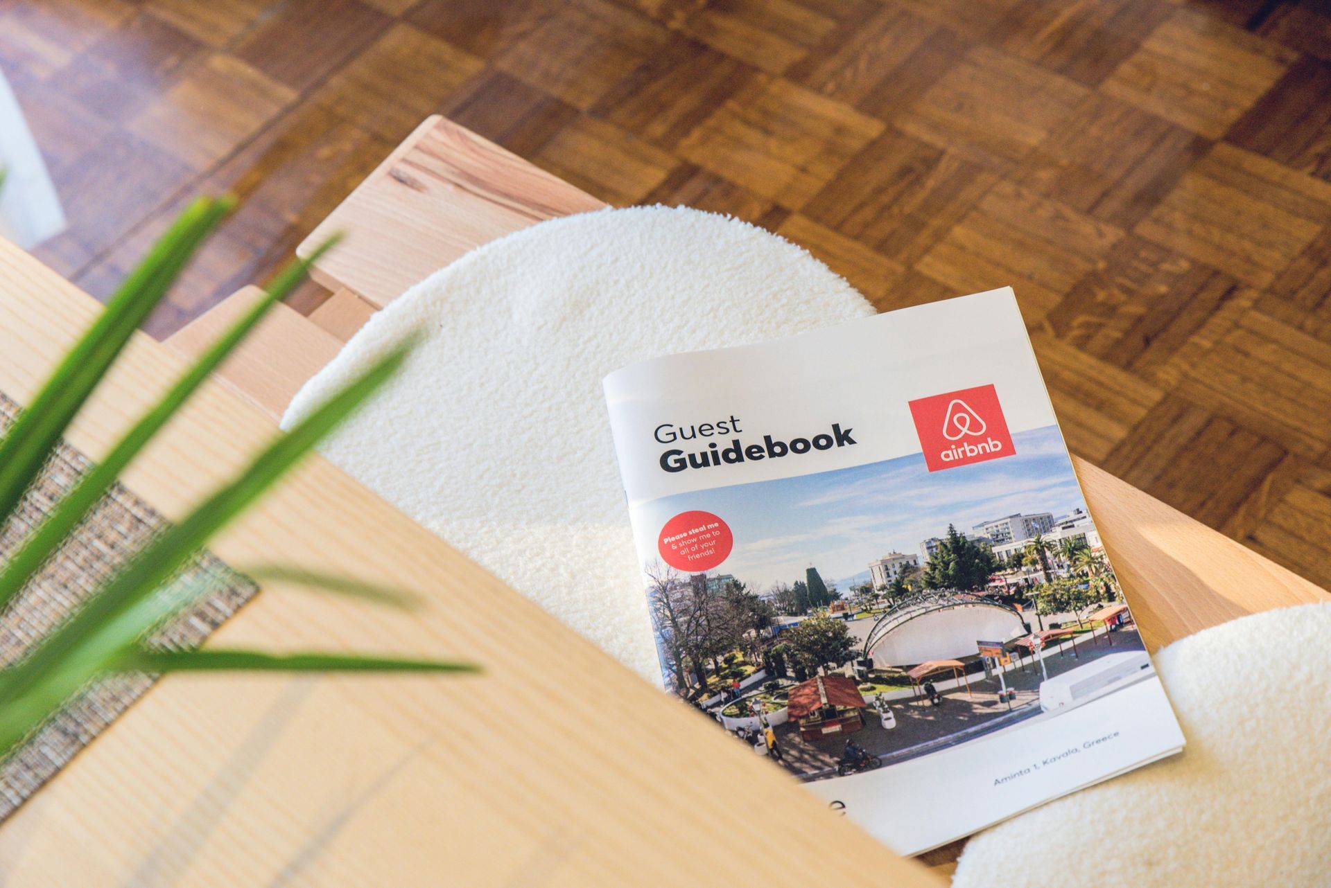 Travel guidebook on a wooden table with a white chair and green plant in the background