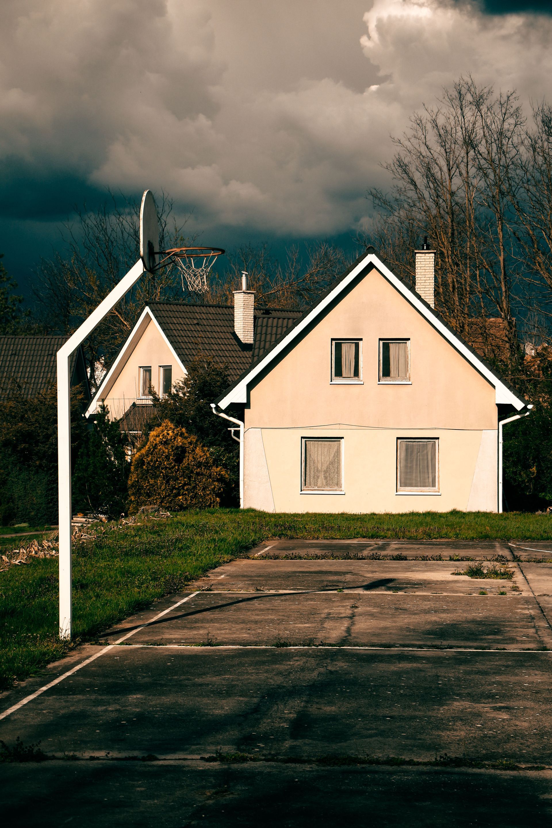 Two cream-colored houses beside a paved road under dark cloudy skies