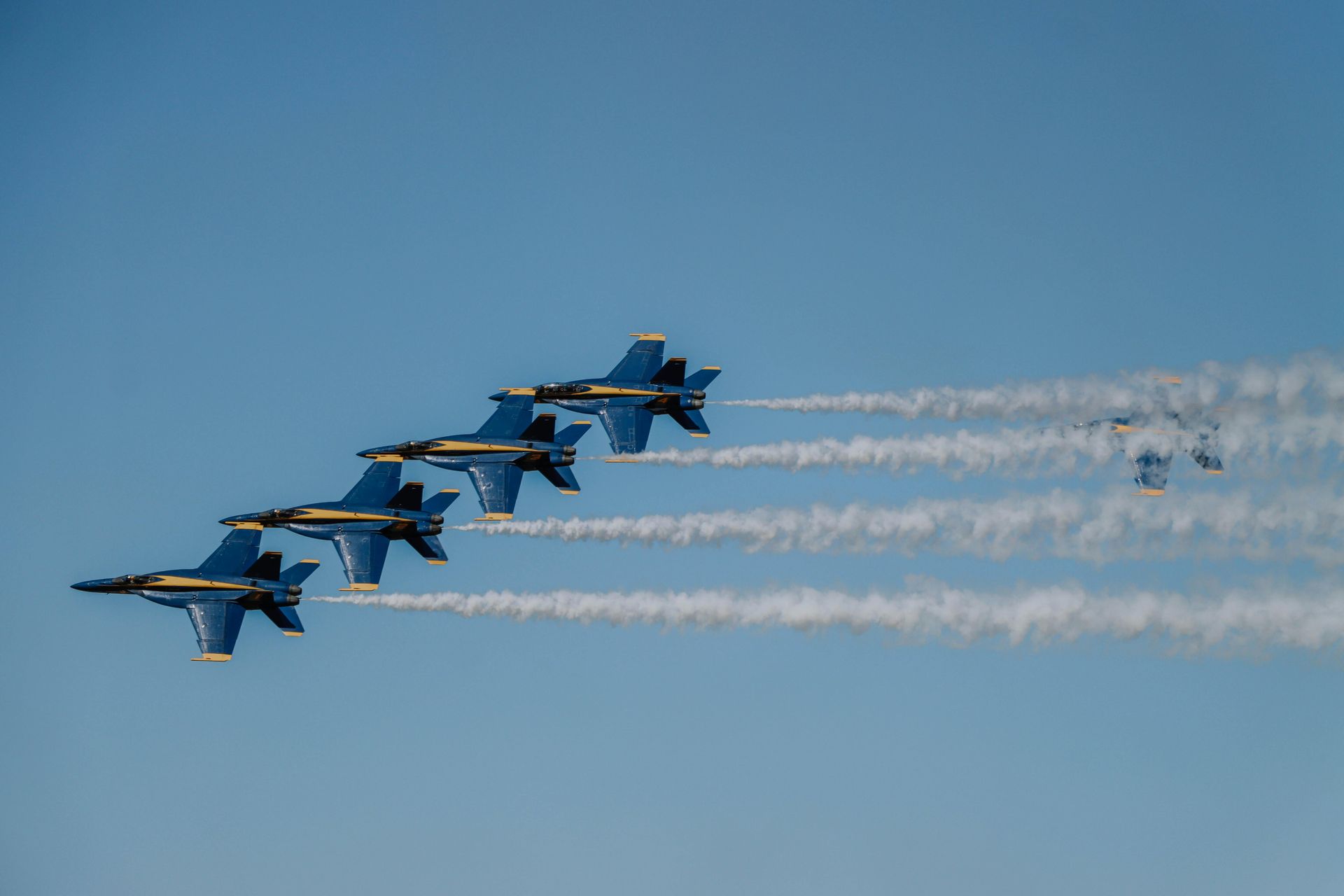 Four blue fighter jets flying in formation, leaving white smoke trails against a clear sky
