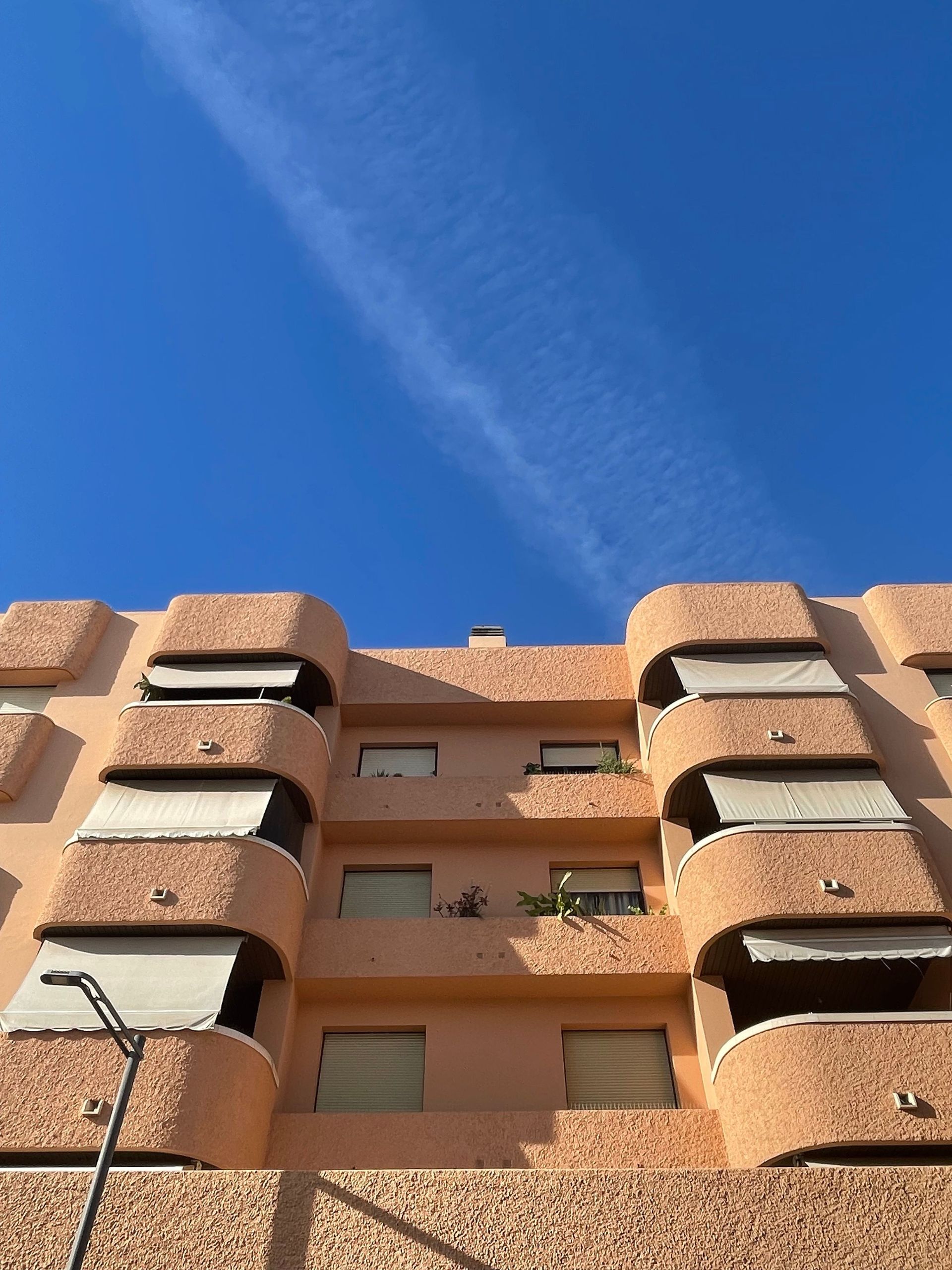 Low-angle view of a peach apartment building against a bright blue sky