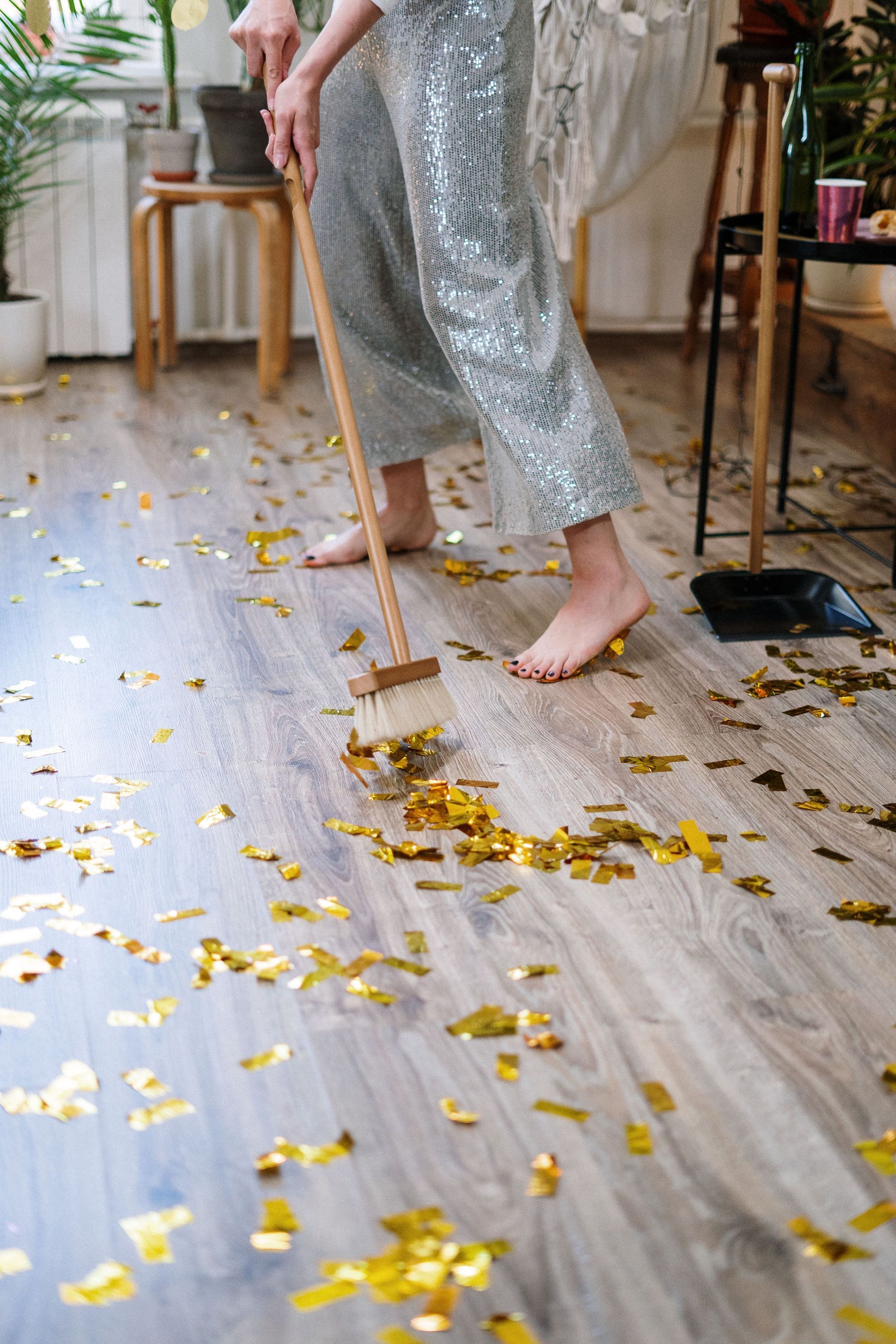 Person sweeping gold confetti from a light wood floor indoors