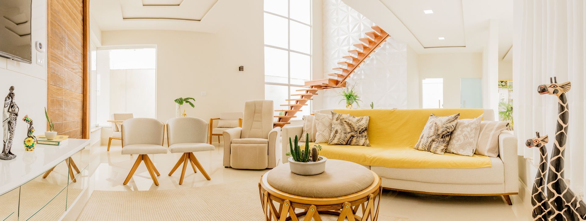 Bright modern living room with white sofa, yellow accents, wood staircase, and coffee table with plants