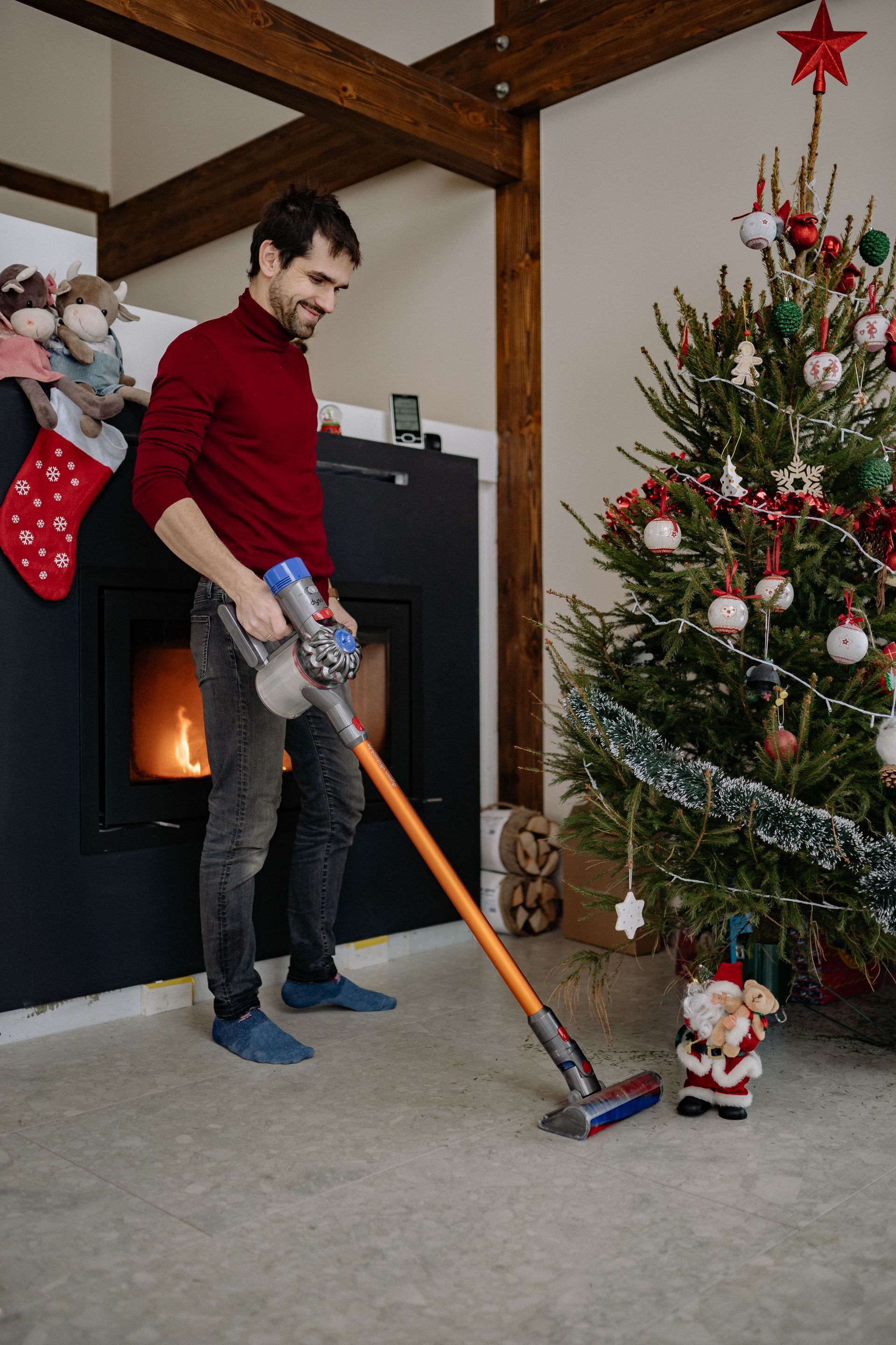 Man vacuuming a carpet beside a decorated Christmas tree and lit fireplace