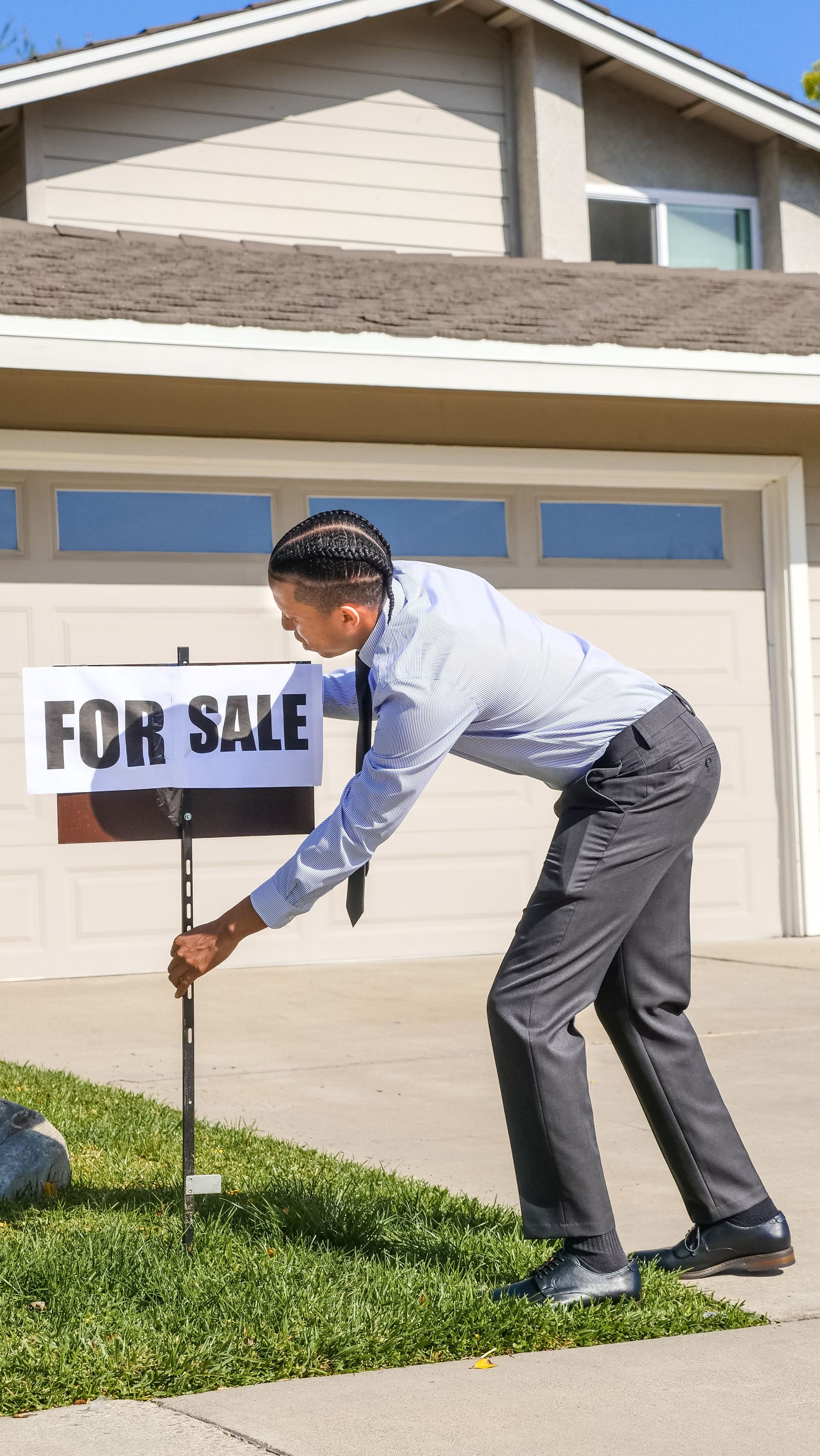Man placing a “FOR SALE” sign in the front yard of a suburban house