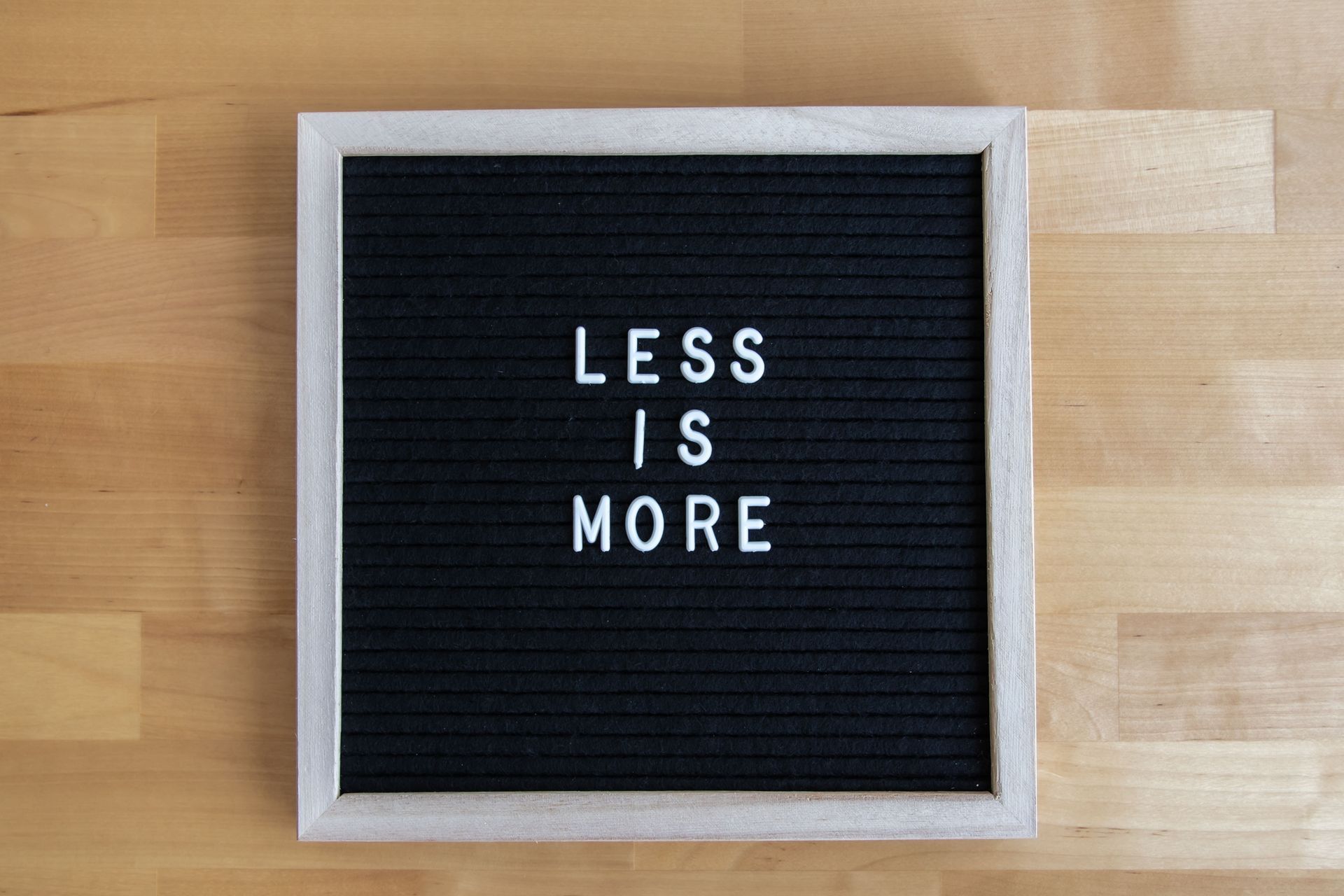 Black letter board on a wooden table reading “LESS IS MORE” in white letters