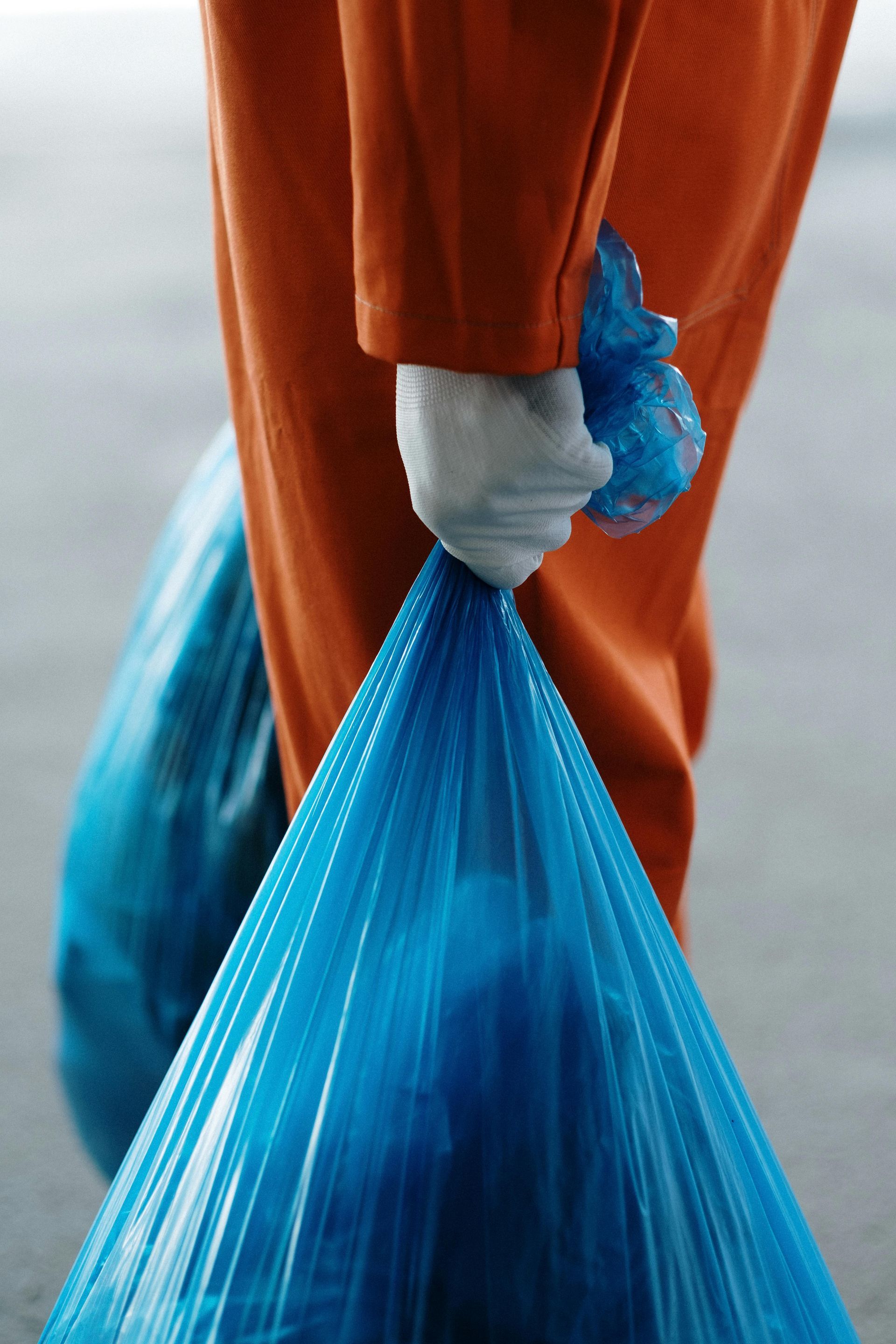 Gloved hand holding a blue plastic bag beside orange pants