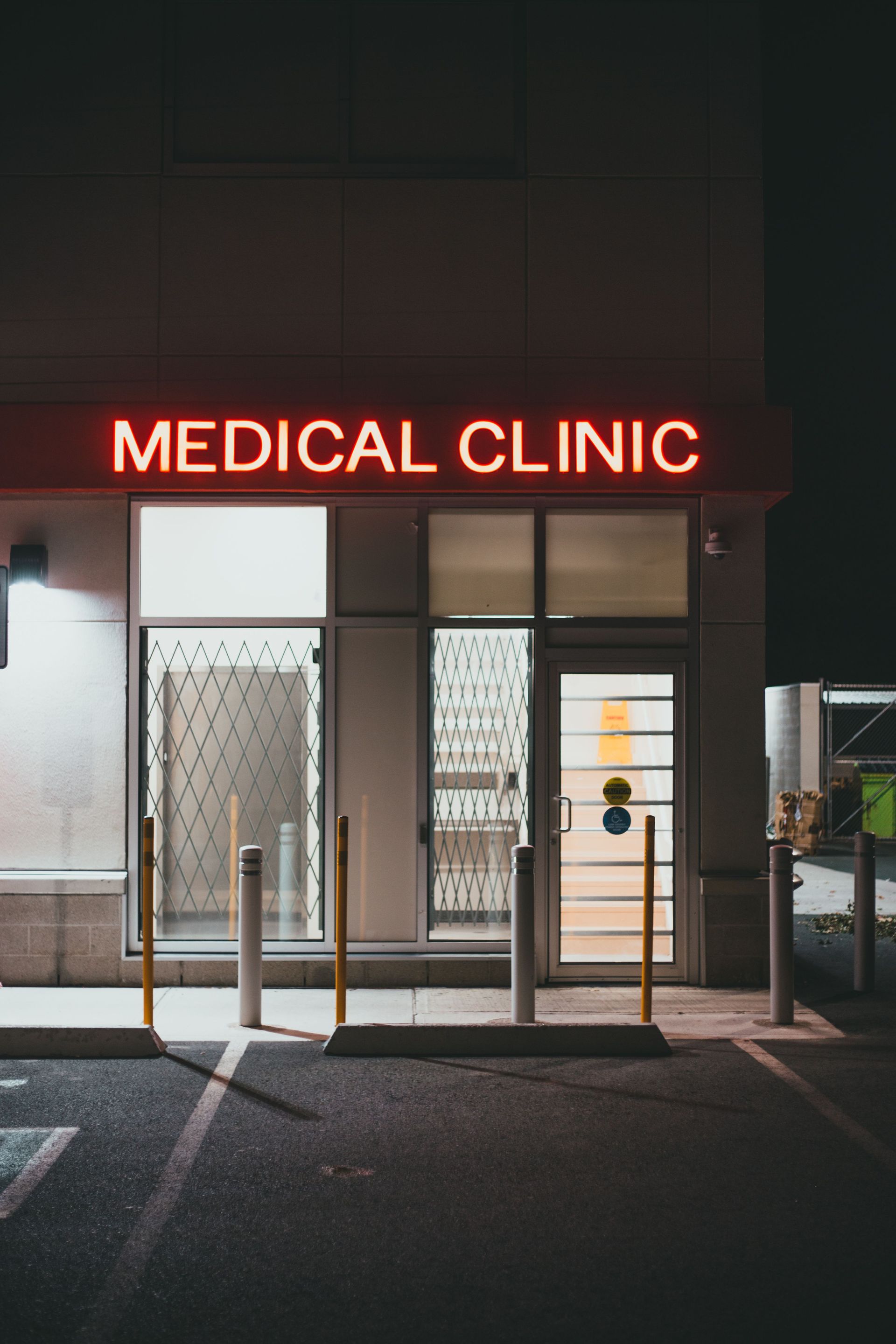 Neon-lit medical clinic entrance at night with glass doors and a red sign.