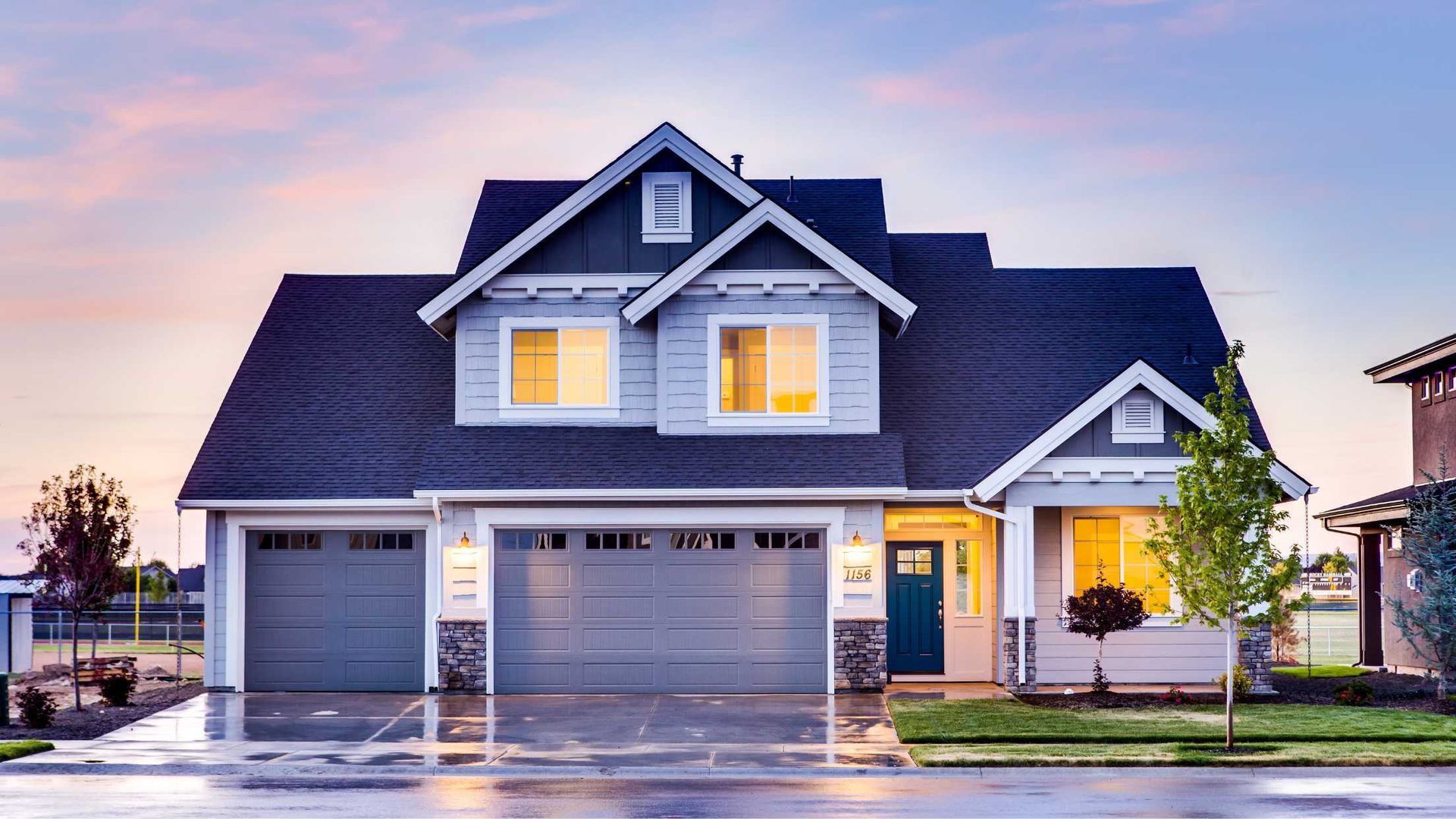 A two-story house with a blue-gray exterior, a gray garage door, and a turquoise front door; dusk setting.