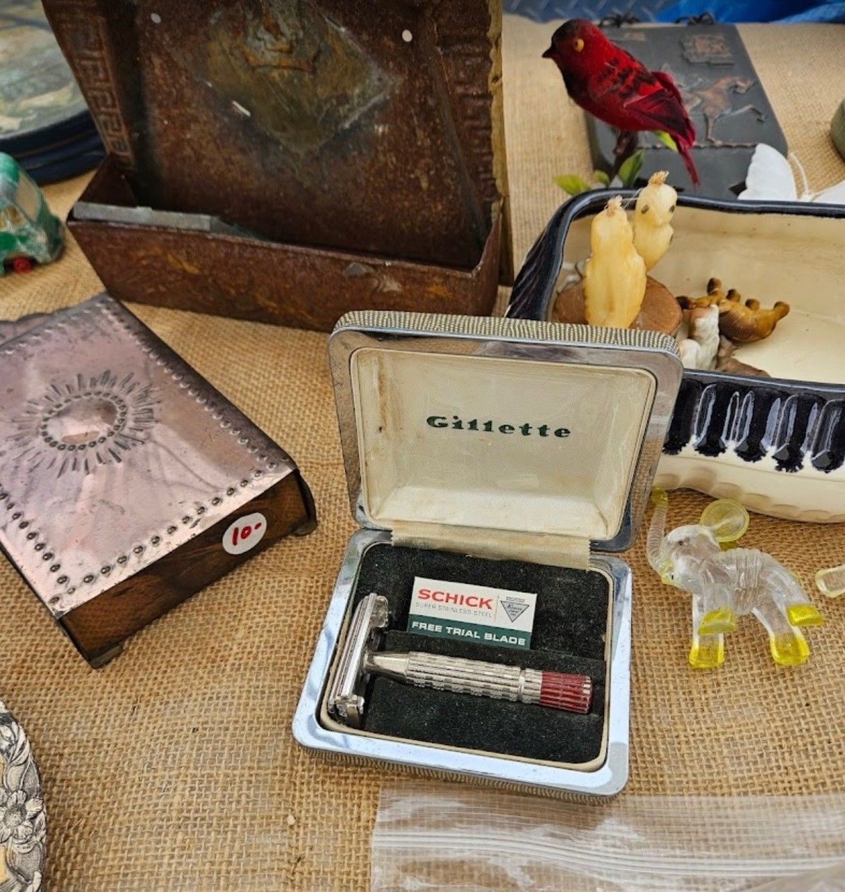 Assorted vintage items on burlap, including an open cigarette case, a small red bird figurine, and a decorative box.